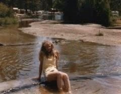Old faded image of a young girl sitting on a wall in a stream