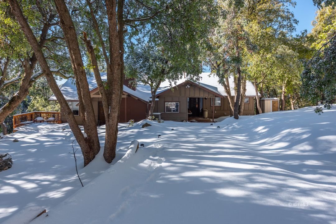 A brown house surrounded by snow-covered ground and trees in a winter setting.