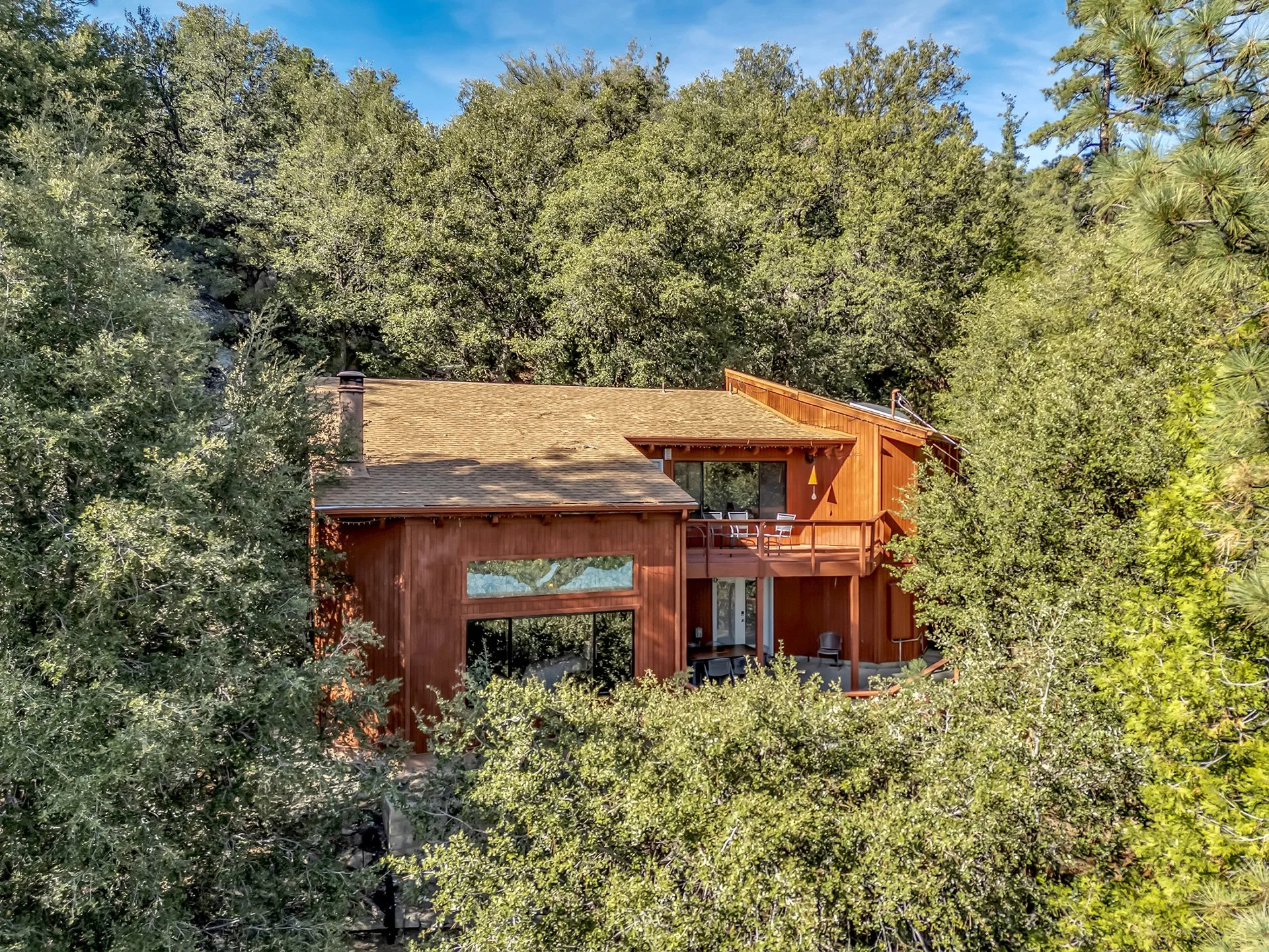A two-story wooden house surrounded by trees with a deck in the back.