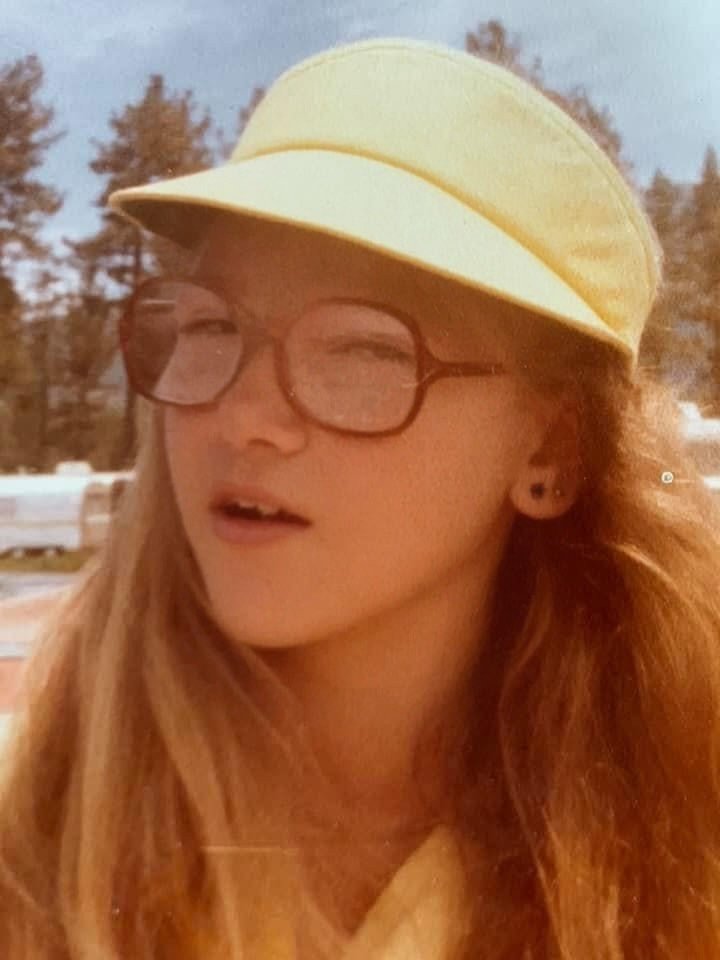 Young girl with glasses and, blonde hair, and a yellow sun visor.