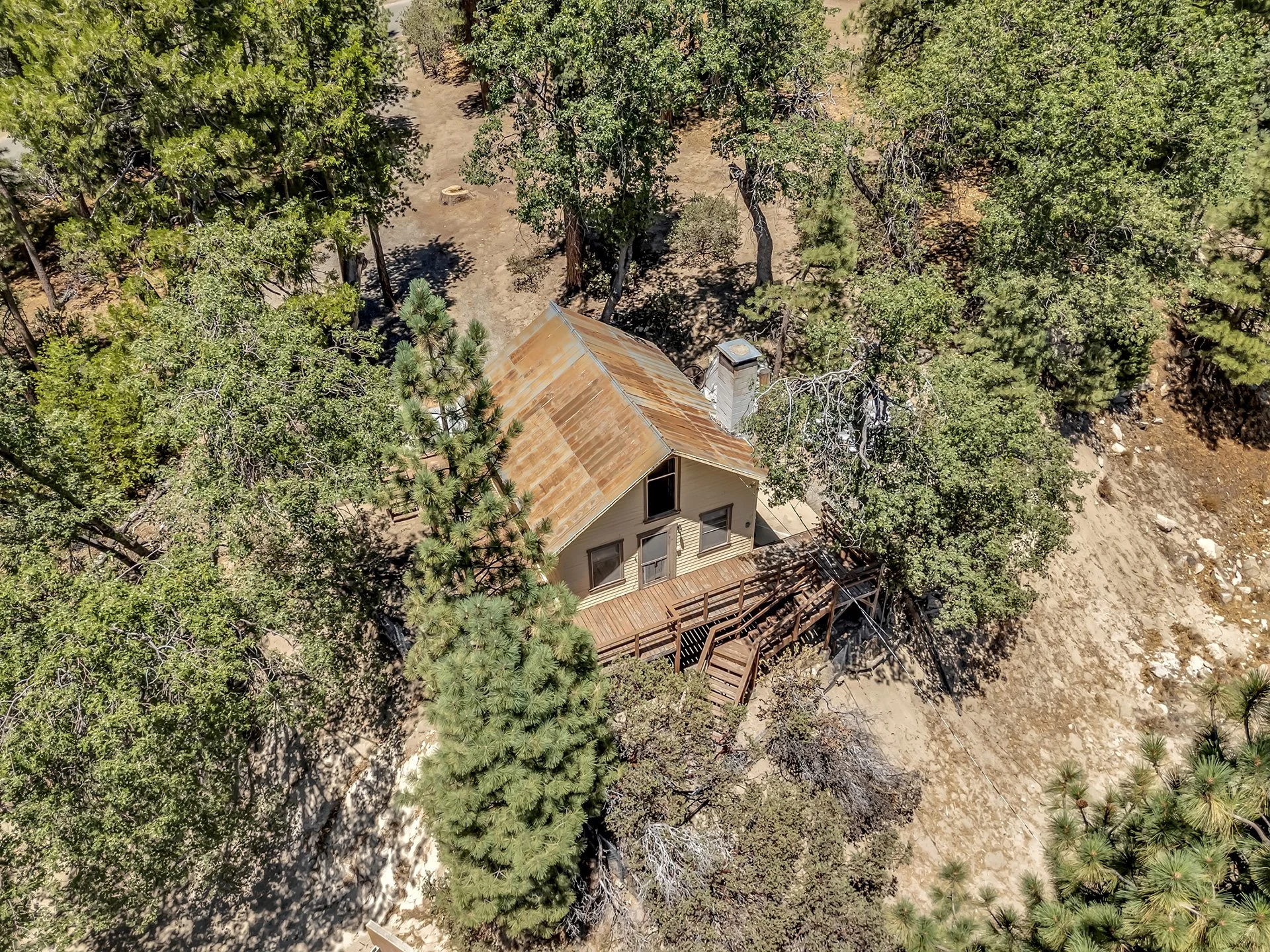 Drone view of fixer cabin with rusted roof surrounded forest