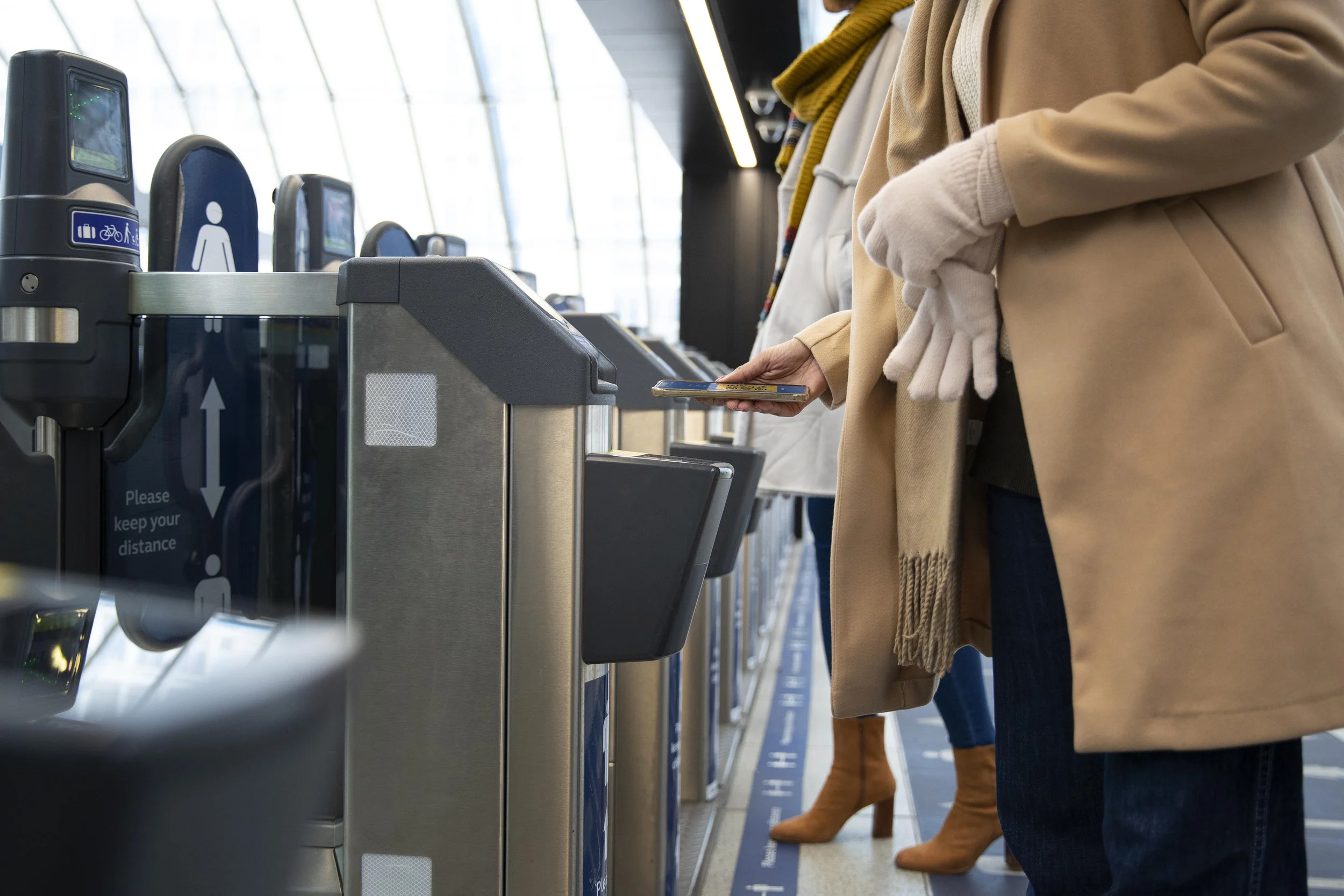 People standing in line at an airport check-in kiosk, with one person holding a phone, in a modern airport terminal.