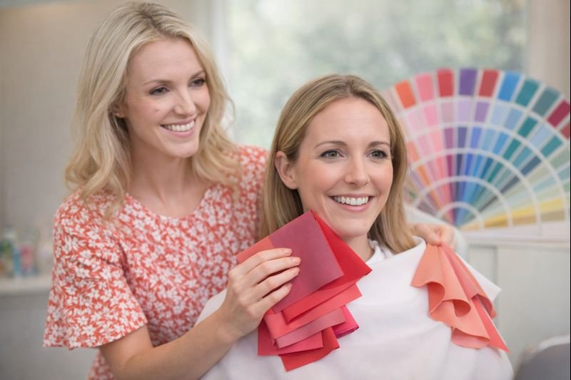 Two women in a salon, one wearing a white cape and the other holding color swatches, with a color fan in the background. Colour analysis. Auckland. Wanaka