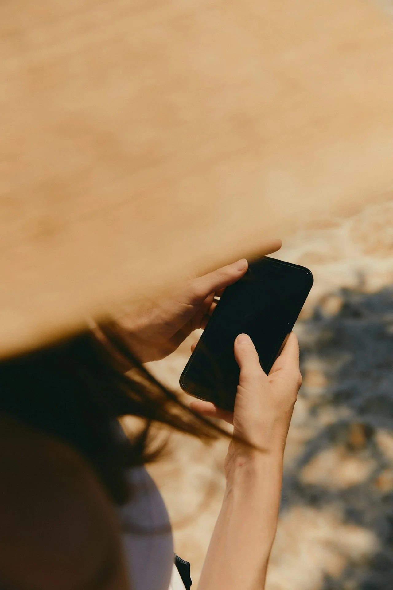 Person holding a smartphone outdoors, beach and rocks in the background.