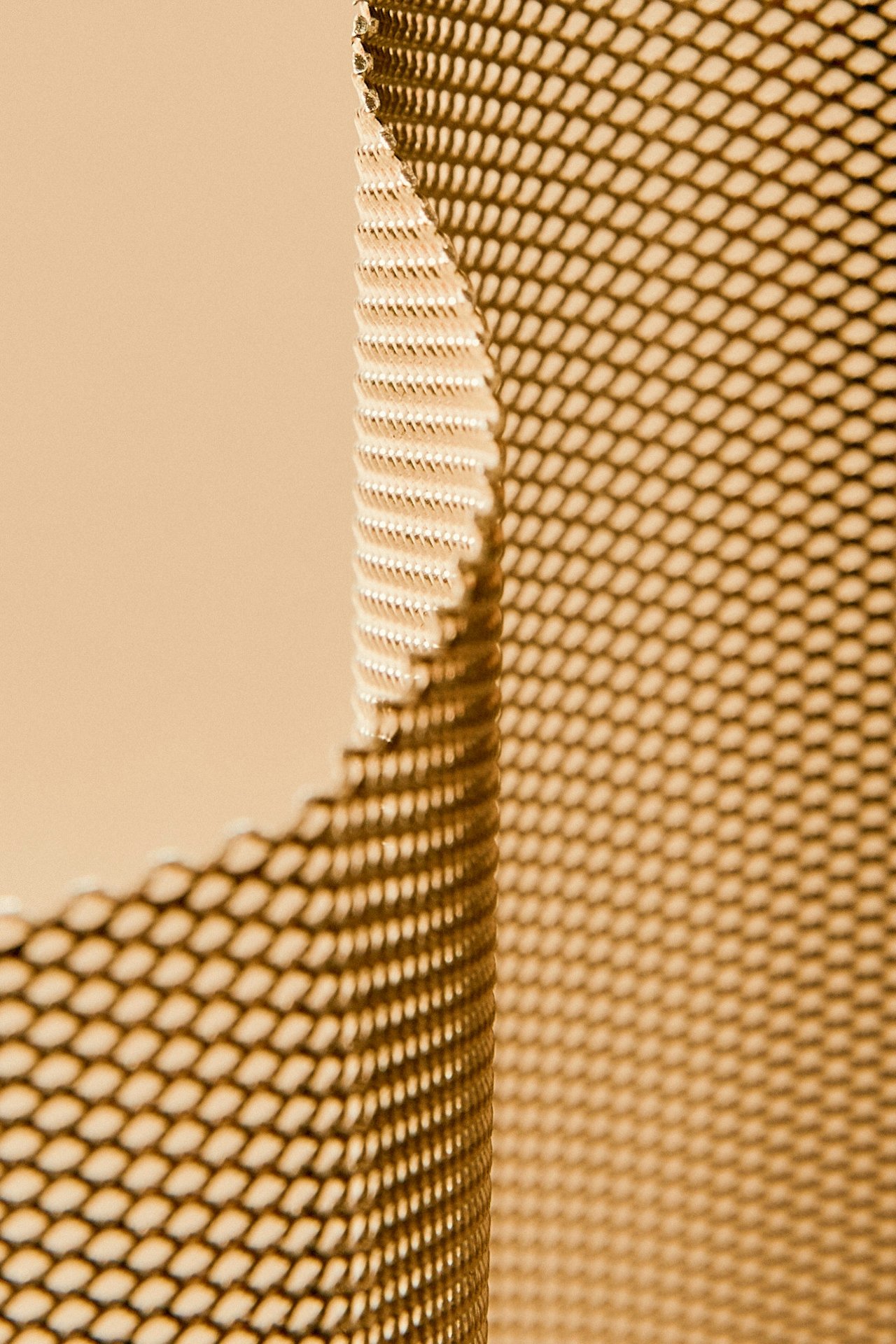 Close-up of a metallic mesh or grid with a curved shape and a beige background