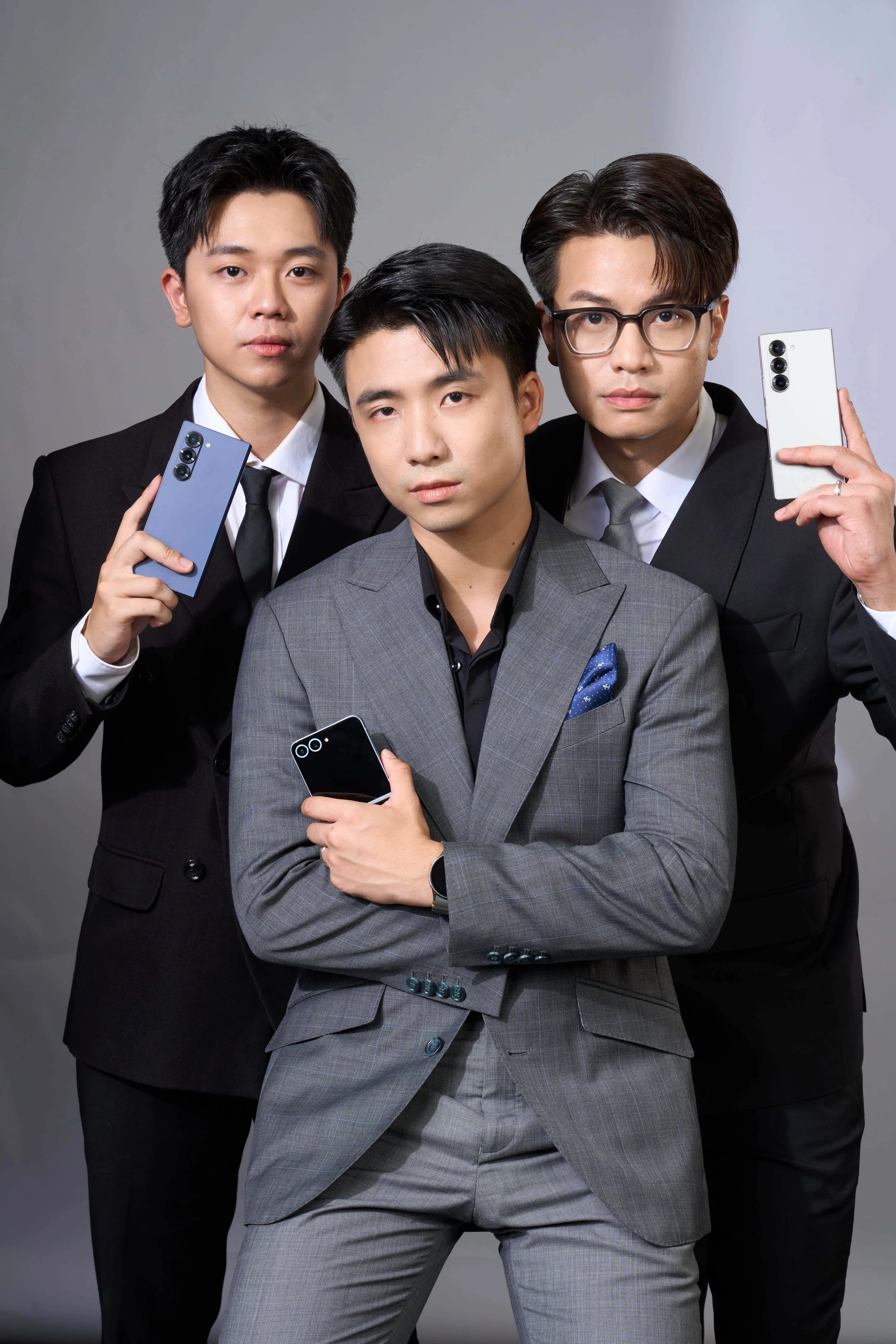 Three men in suits holding smartphones against a plain gray background.