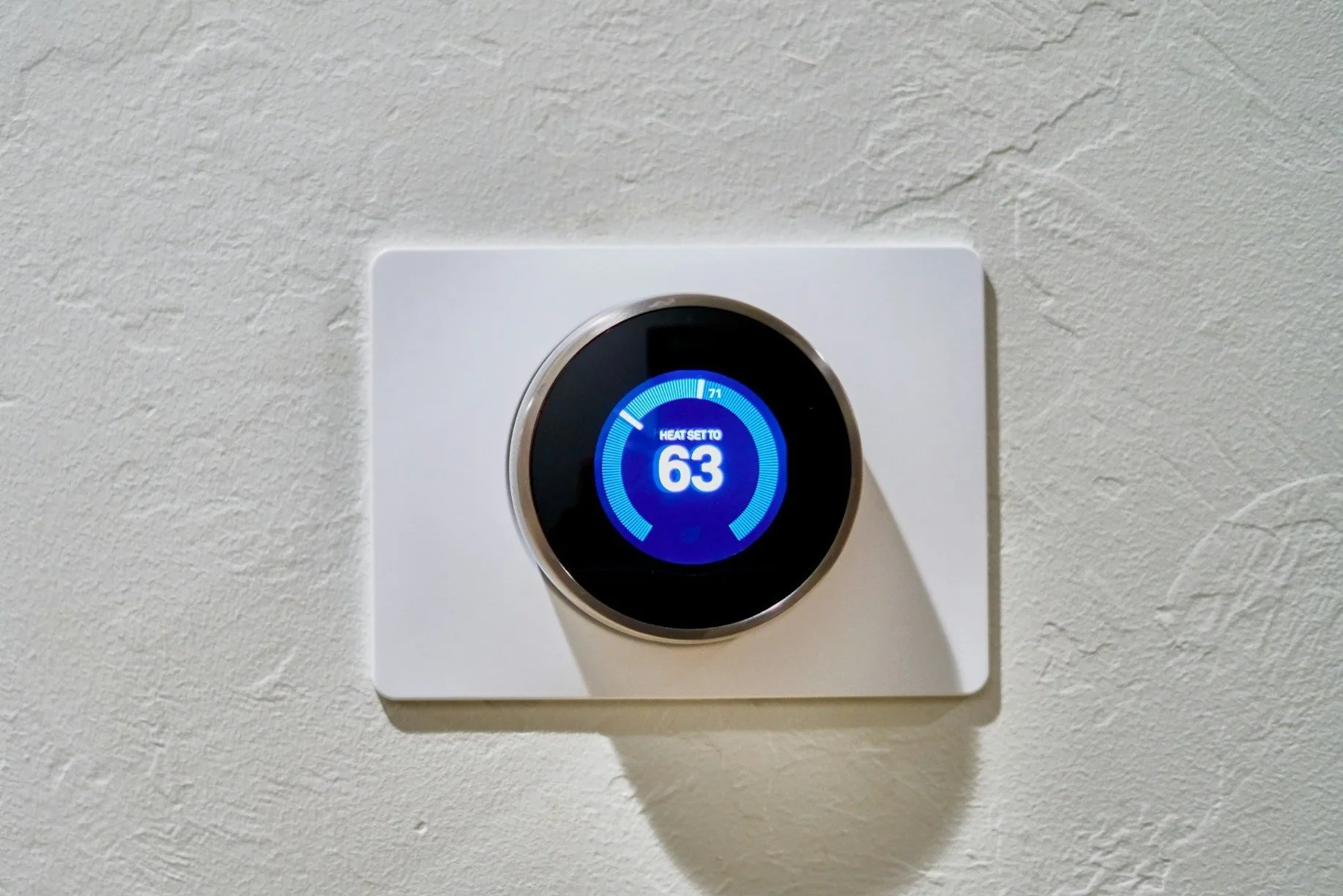 Digital thermostat on a white wall showing a temperature of 63 degrees.
