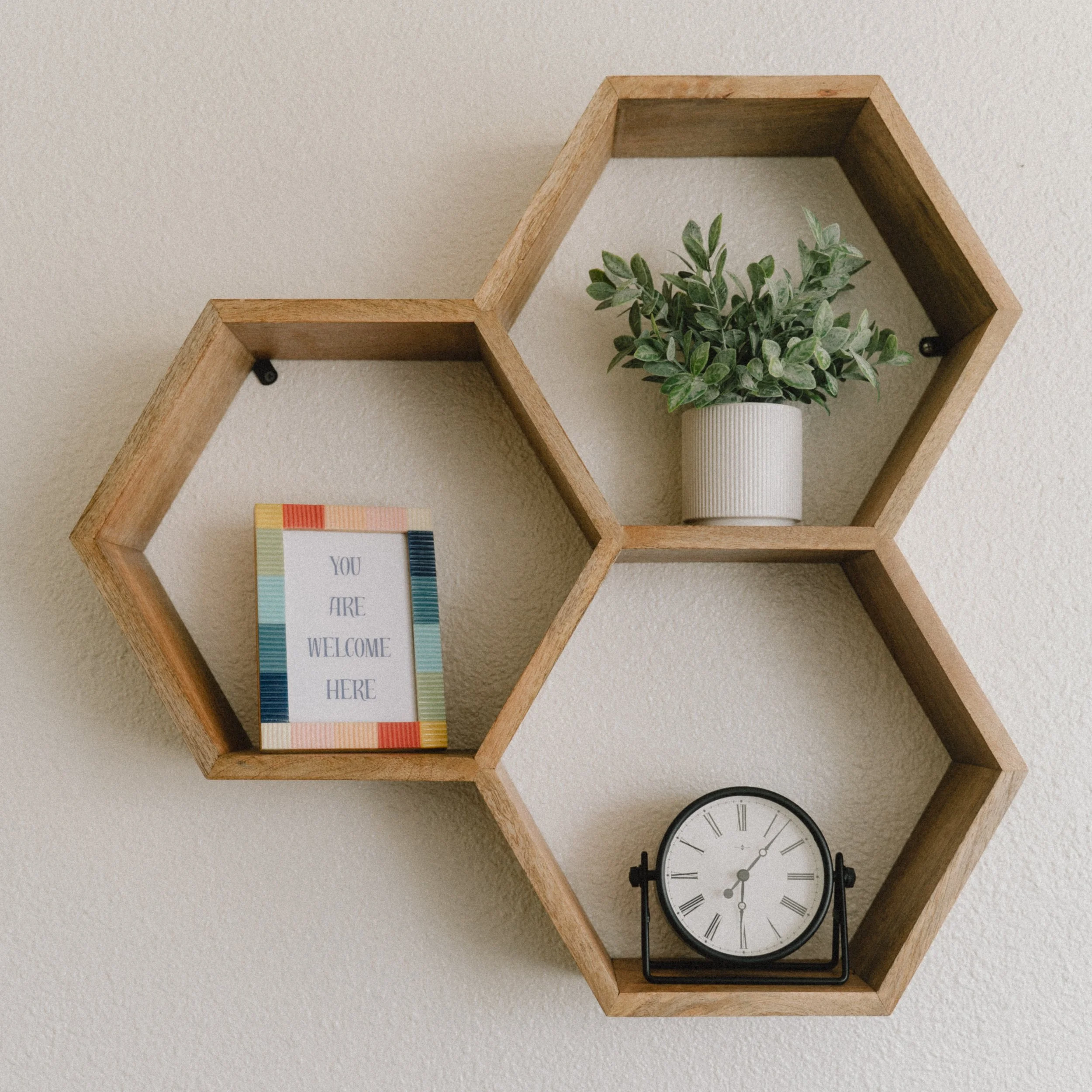 Three geometric shelves with a clock, a plant, and a frame saying "You are Welcome Here"