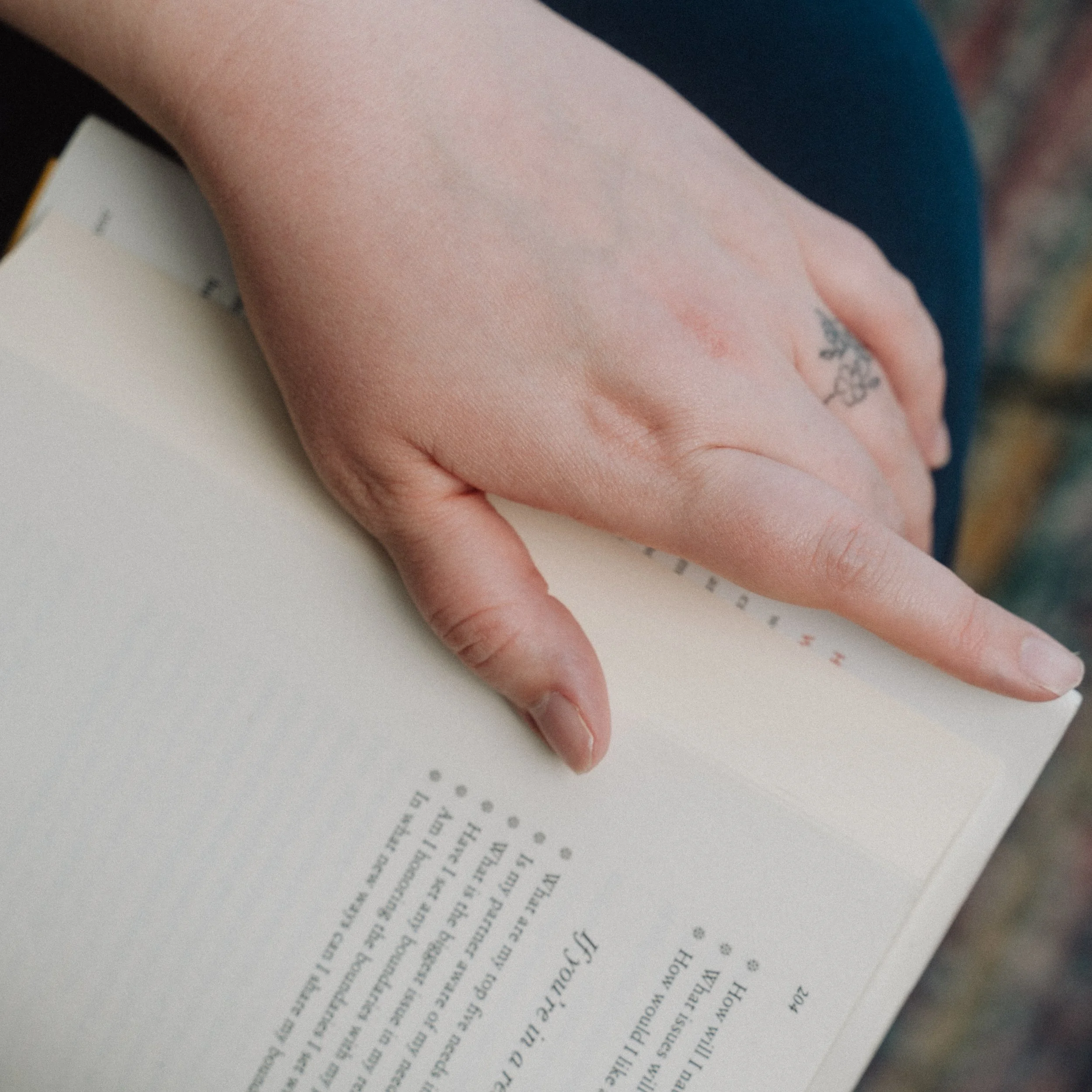 A person's hand resting on an open book or document, with the index finger pointing to a line of text.