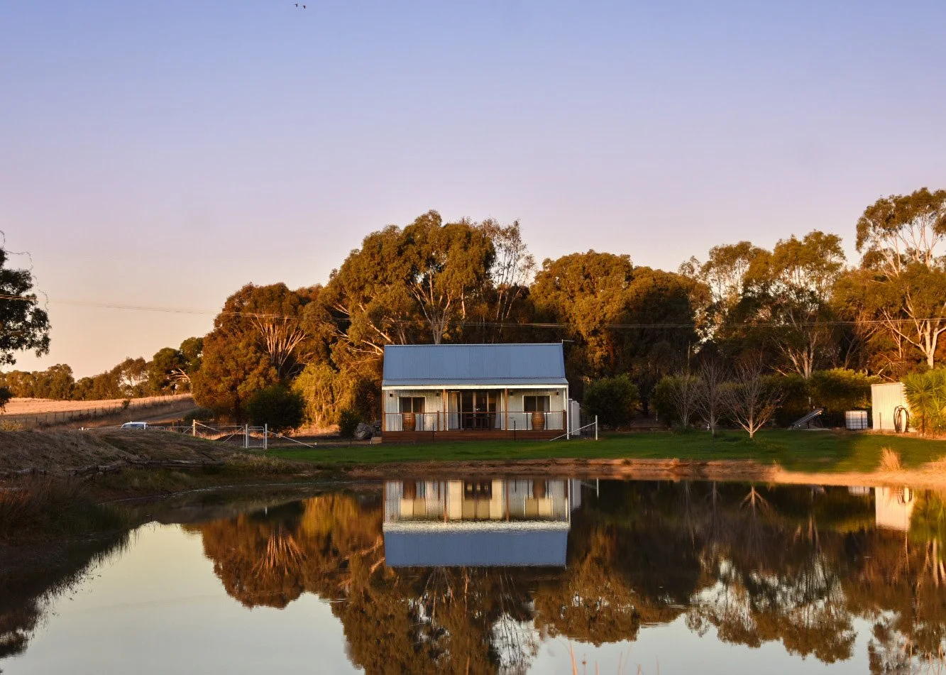 A house near a pond with trees and clear sky at sunset, with the house and trees reflected in the water.