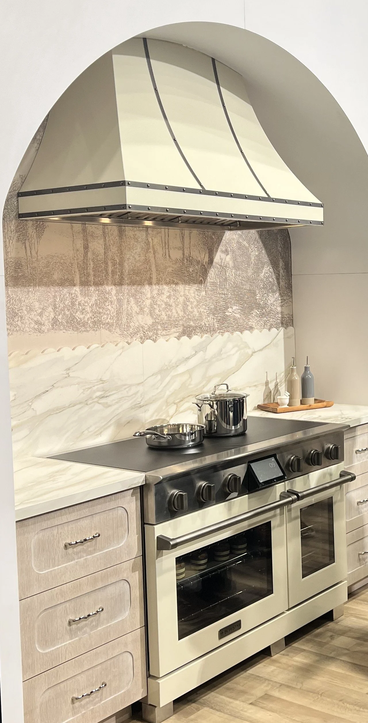 Ivory induction range in an arched alcove with a cream range hood and marble backsplash