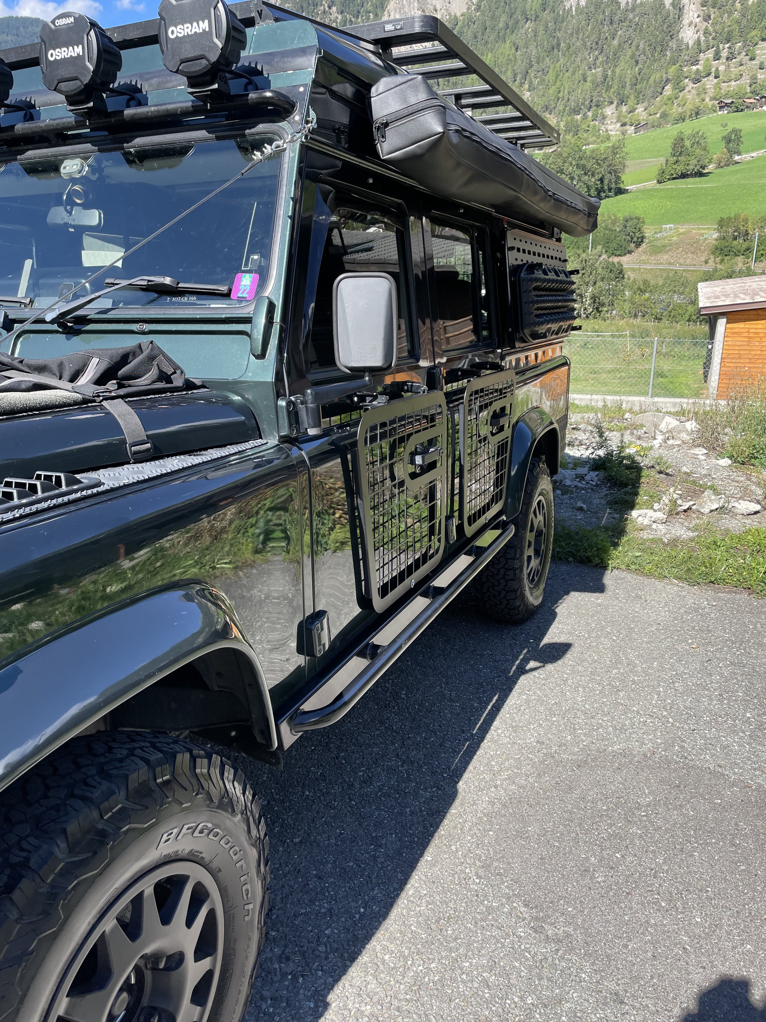 A black off-road vehicle with rooftop gear, mountain terrain in the background, and a shaded side