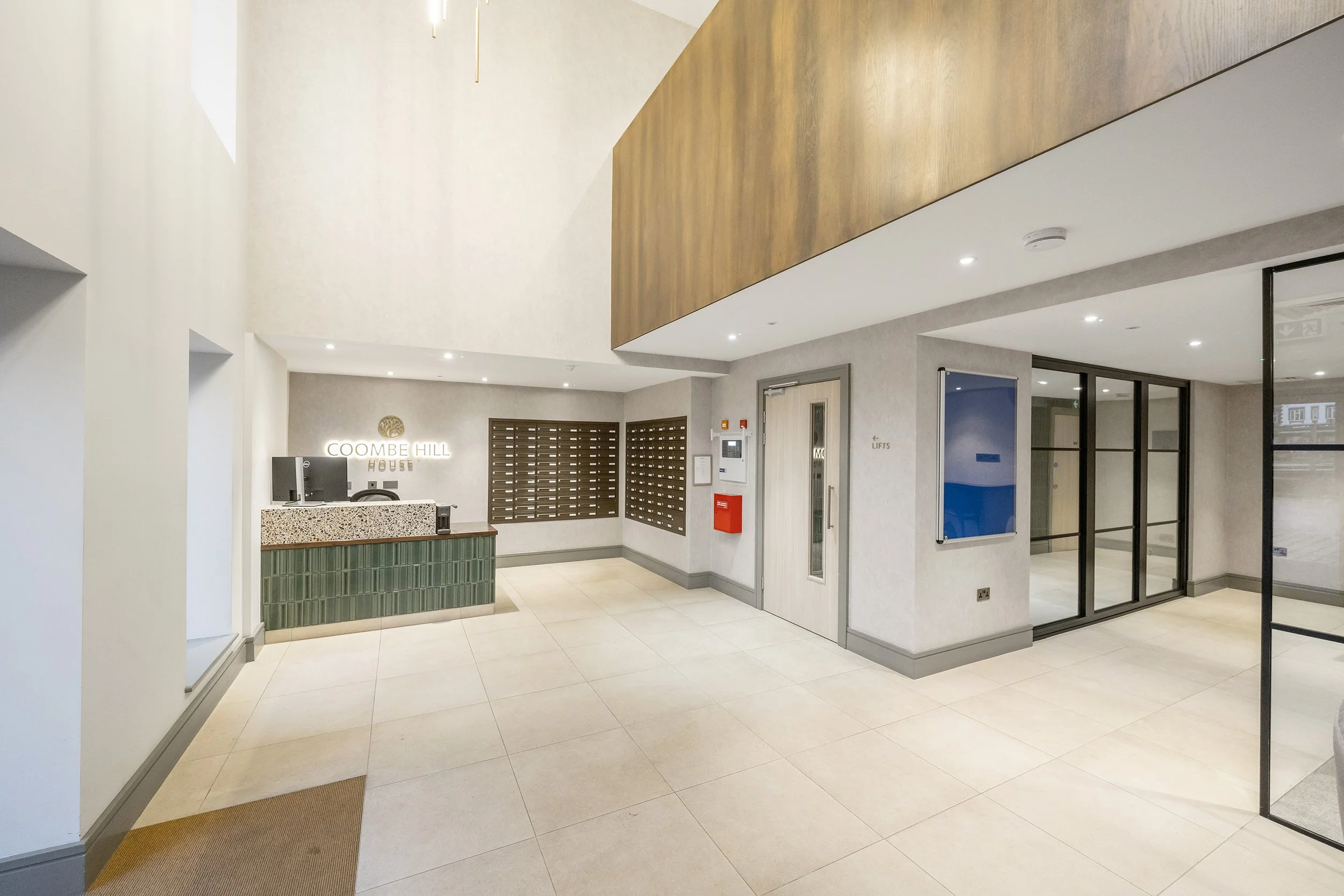Modern hotel lobby with staircase, large windows, seating area, and bar with high stools.