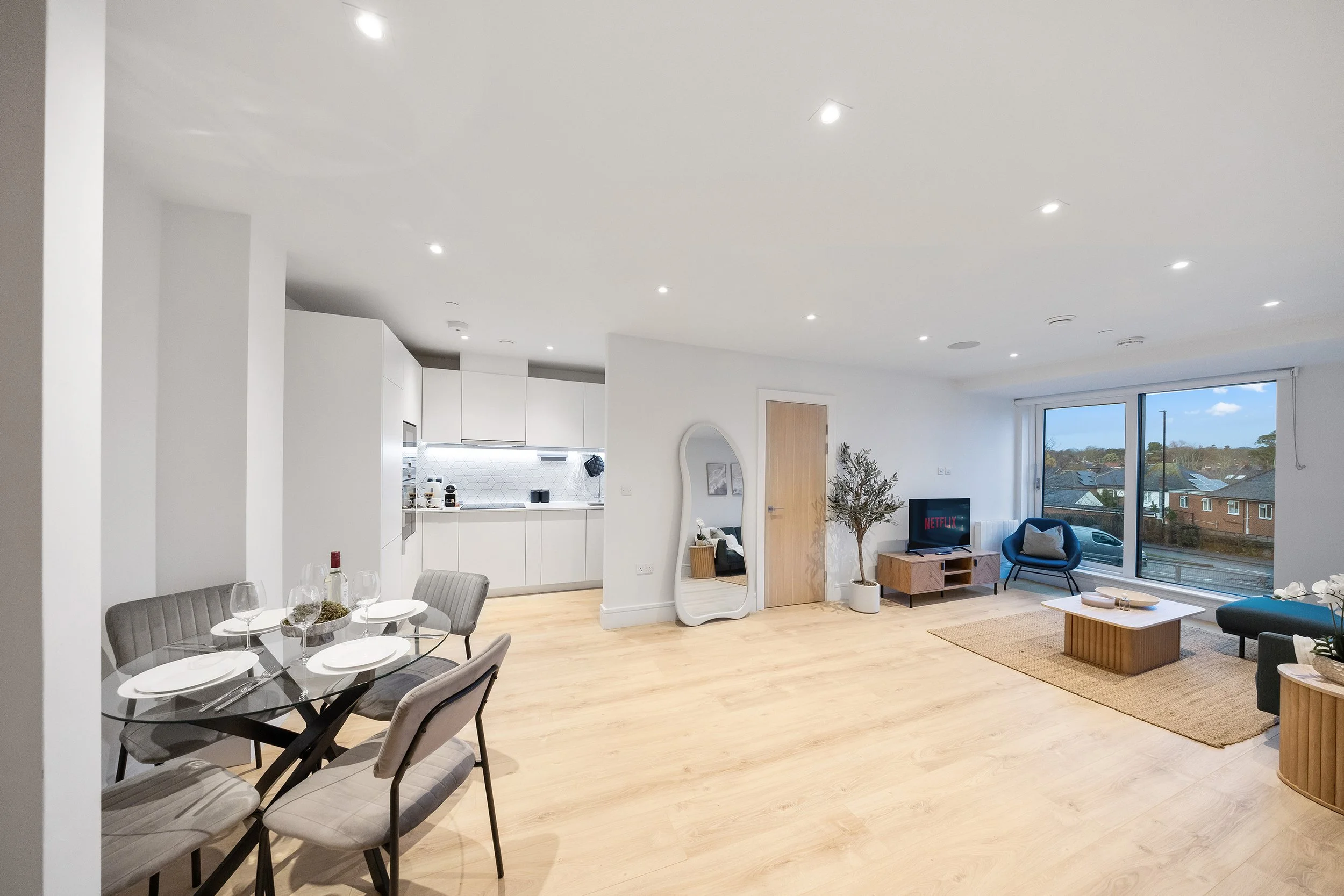 Open plan living room with a luxury feel, four seater sofa and coffee table, armchair, a blanket, a large window with a view of trees