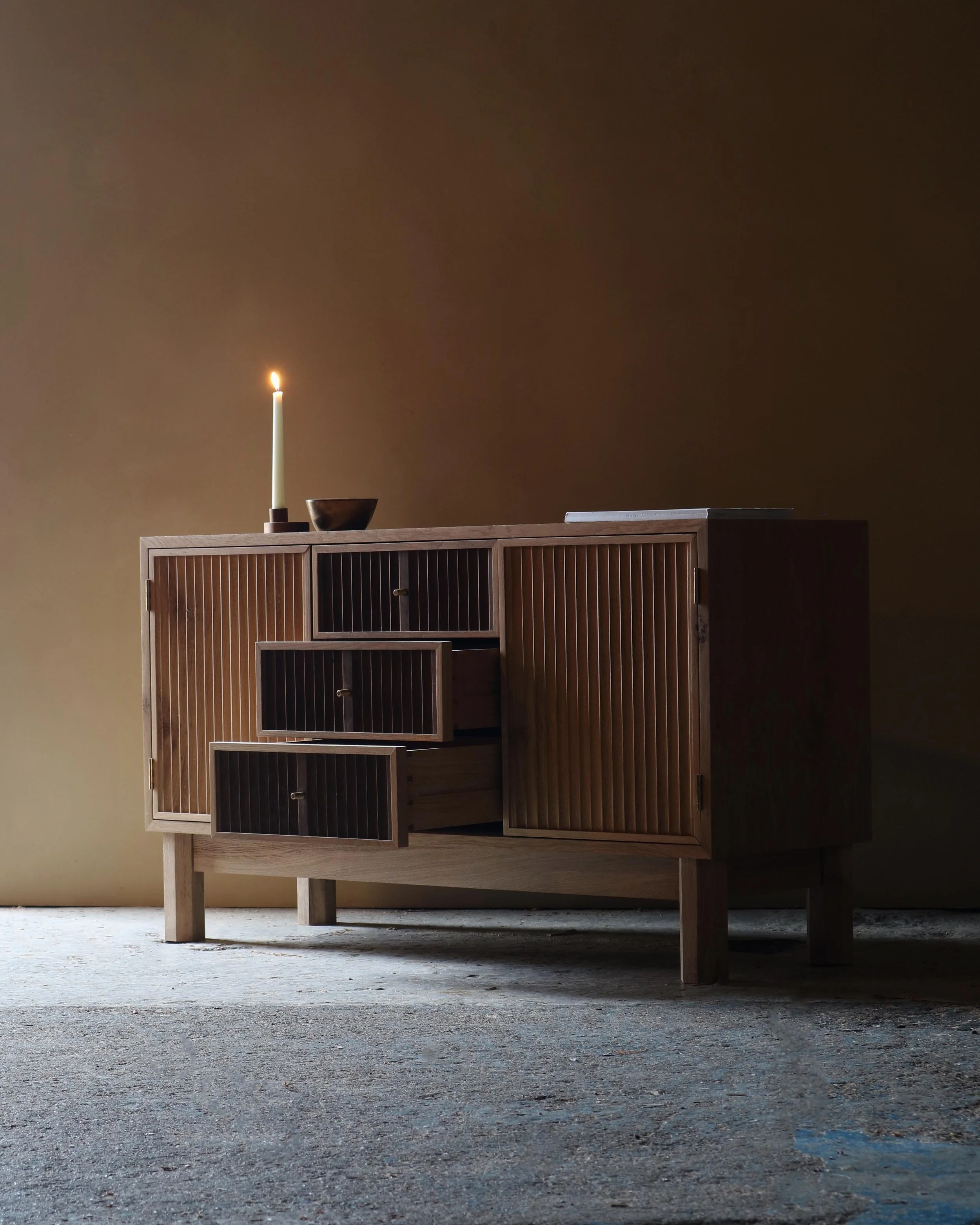 Handcrafted Flauta cabinet in solid oak with fluted front panels, natural and fumed oak contrast, brass detailing, and octagonal legs