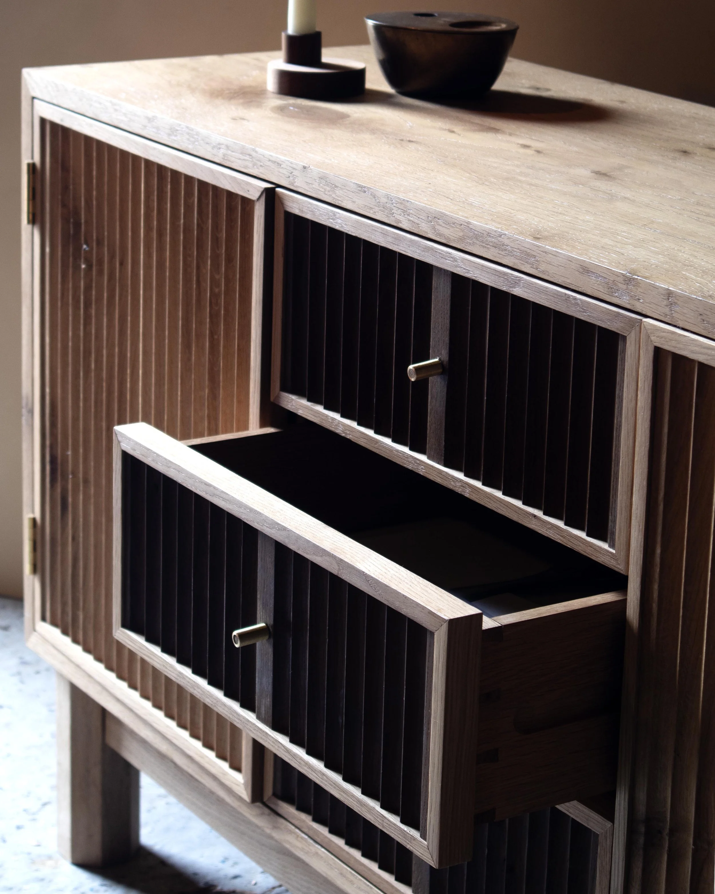 Handcrafted Flauta cabinet in solid oak with fluted front panels, natural and fumed oak contrast, brass detailing, and octagonal legs