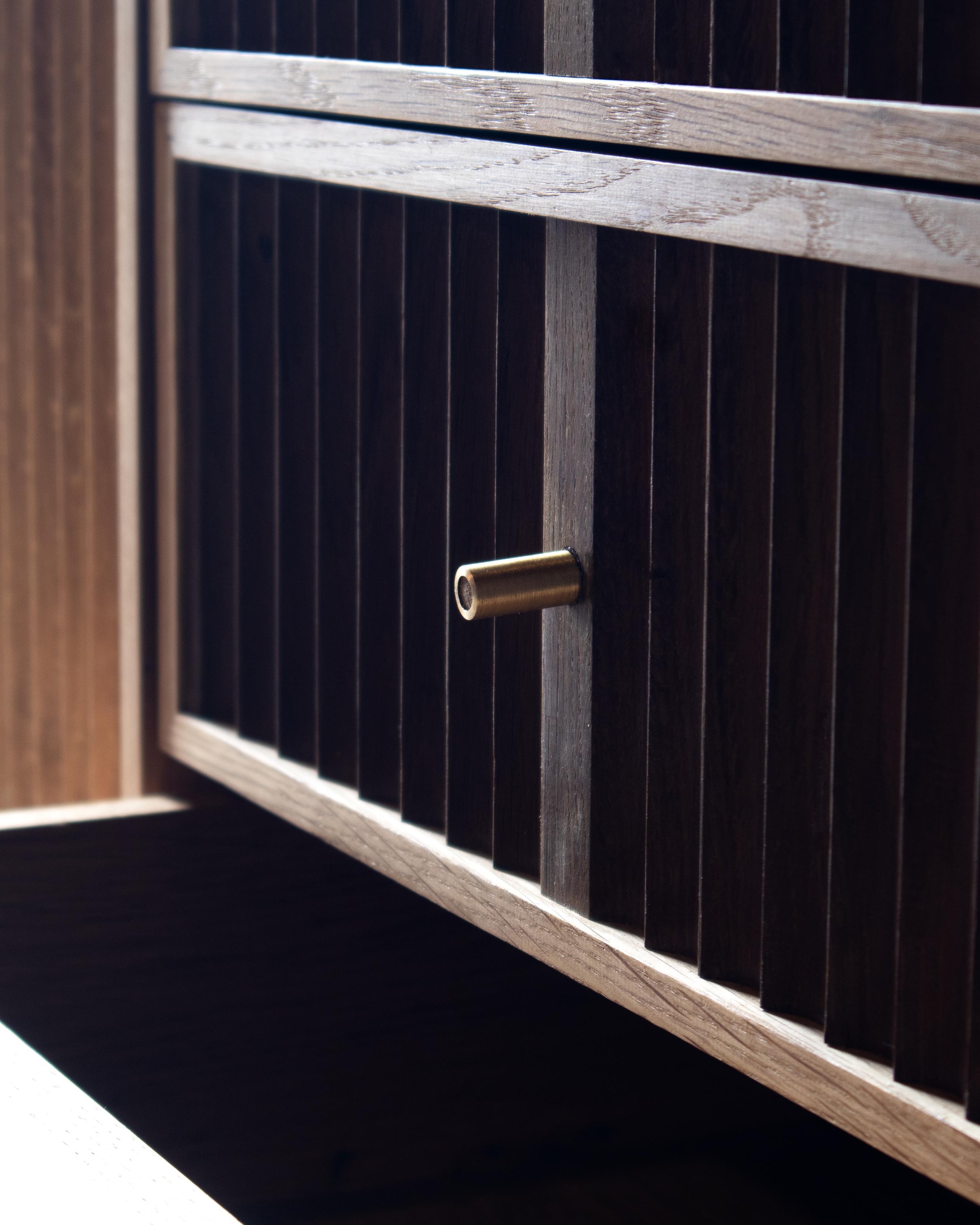 Handcrafted Flauta cabinet in solid oak with fluted front panels, natural and fumed oak contrast, brass detailing, and octagonal legs
