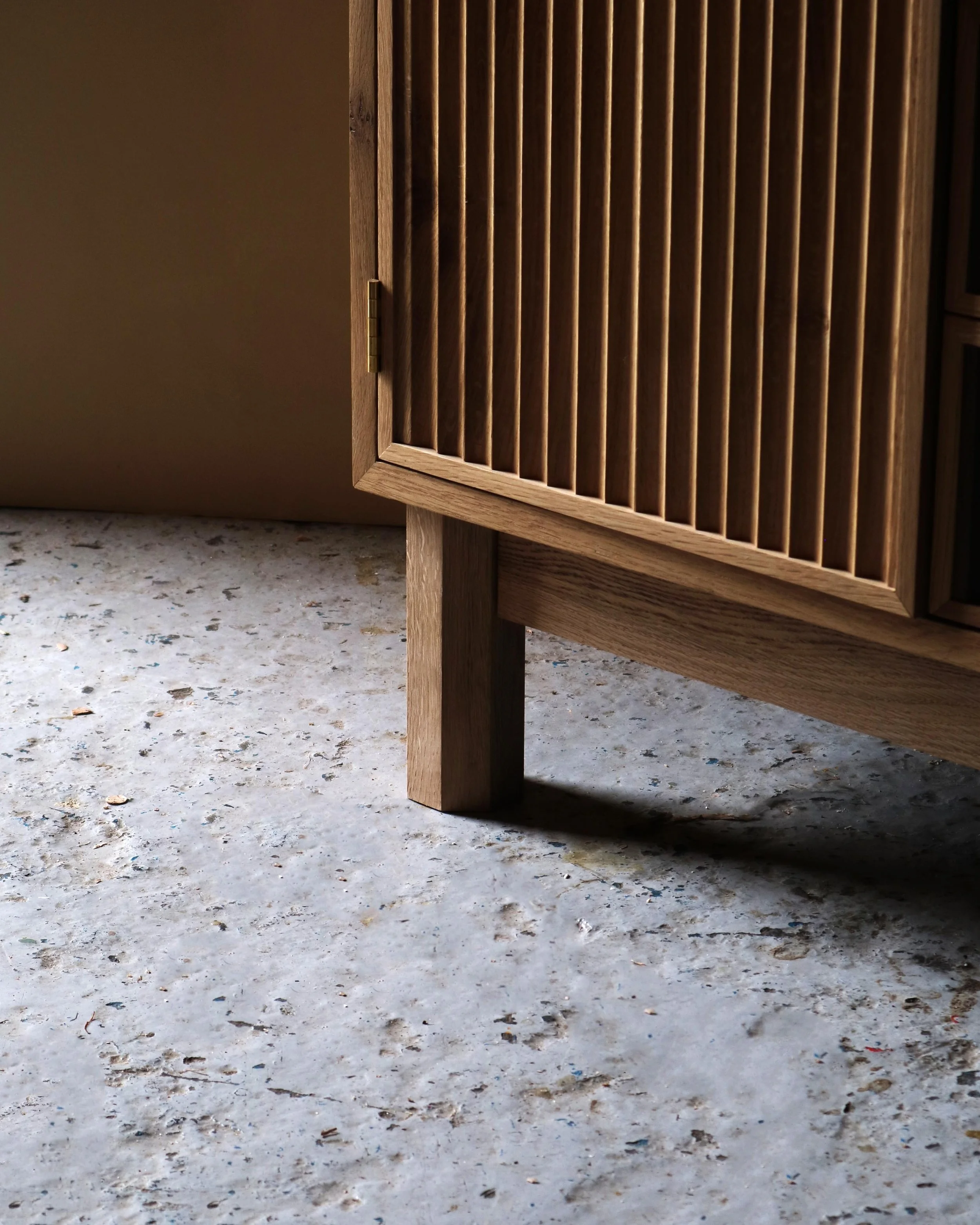 Handcrafted Flauta cabinet in solid oak with fluted front panels, natural and fumed oak contrast, brass detailing, and octagonal legs