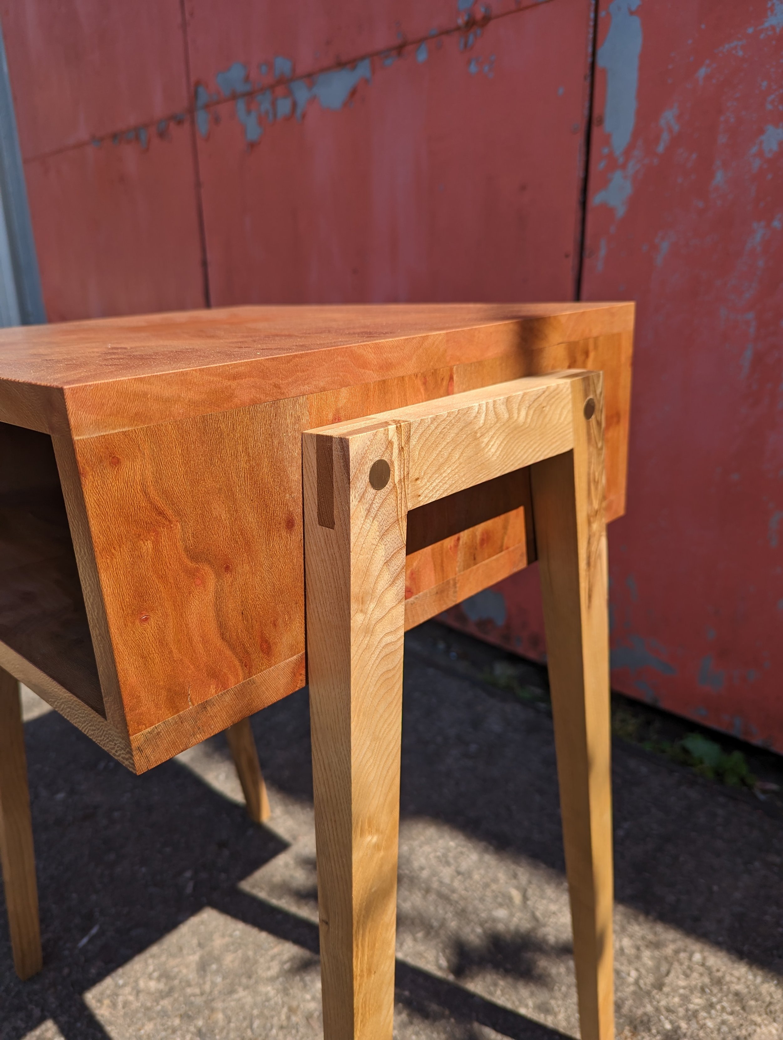 Wooden furniture piece, possibly a table or desk, with a light wood finish, positioned outdoors near a weathered red wall.