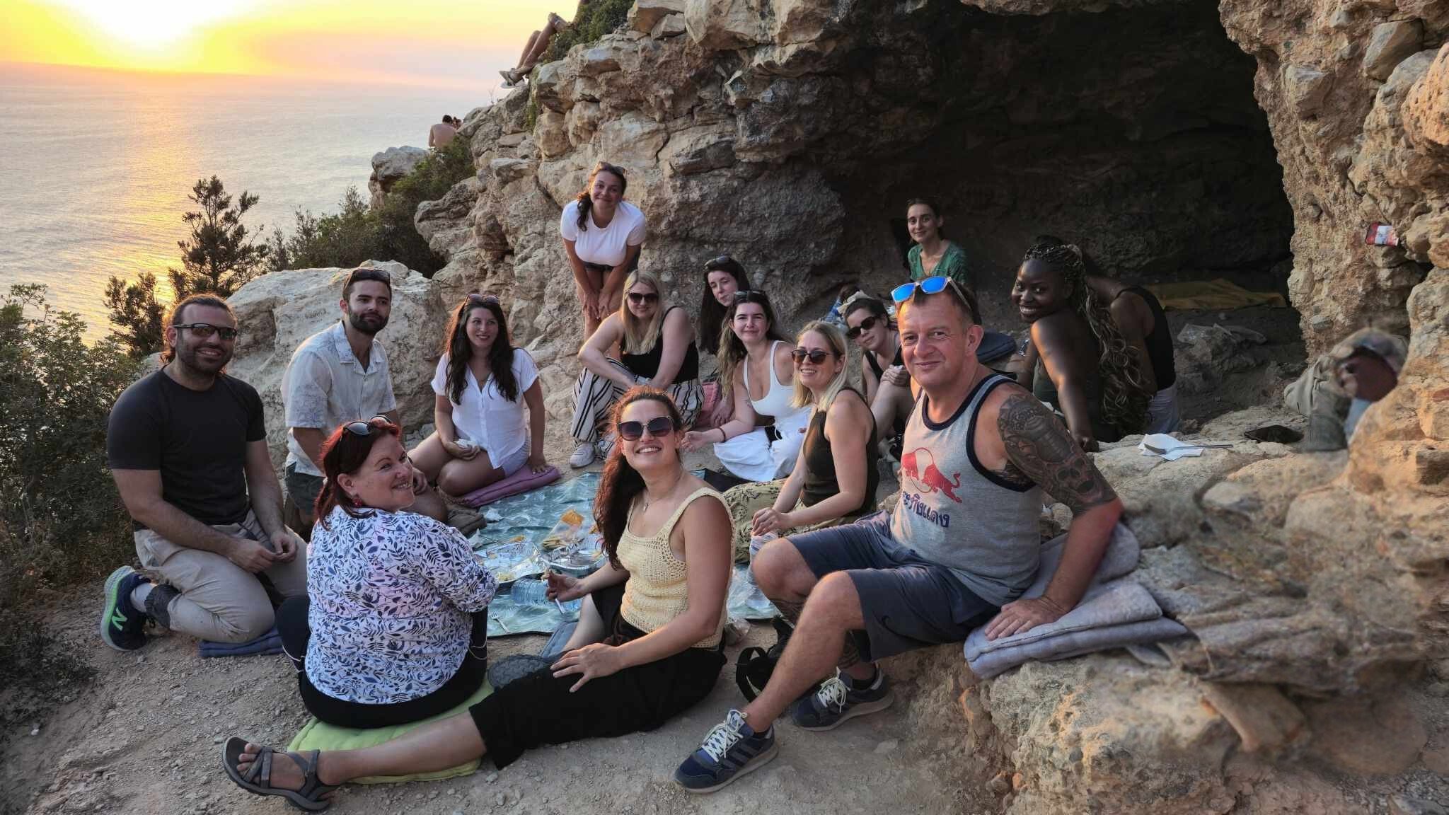 Group of people having a picnic on a rocky cliffside during sunset at the beach.