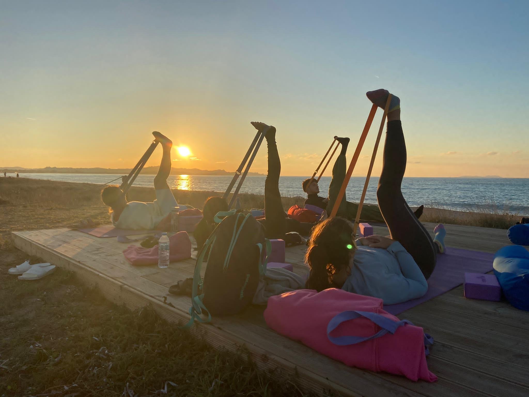 Group of people doing yoga on wooden platform by beach at sunset