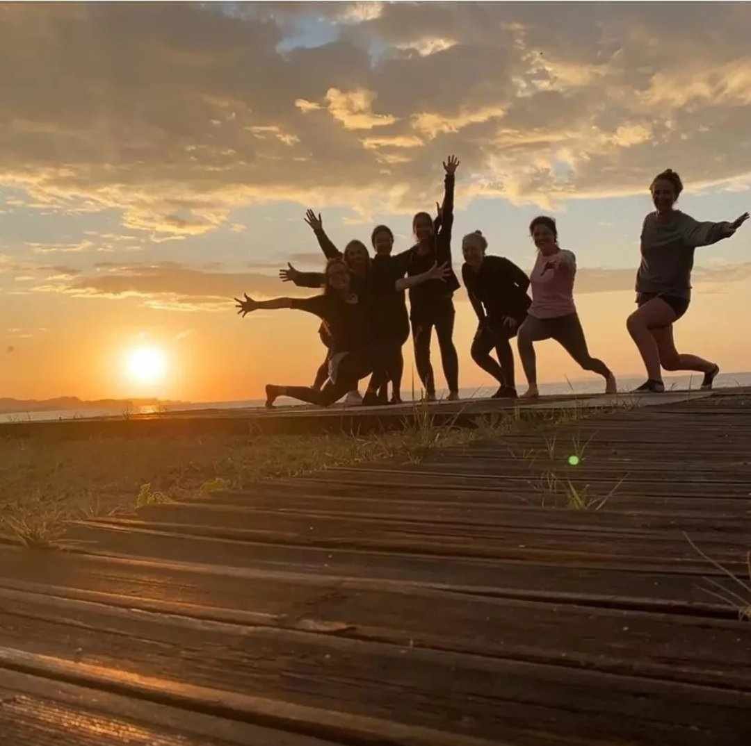 Group of people posing on a boardwalk during sunset with their arms outstretched and smiling.