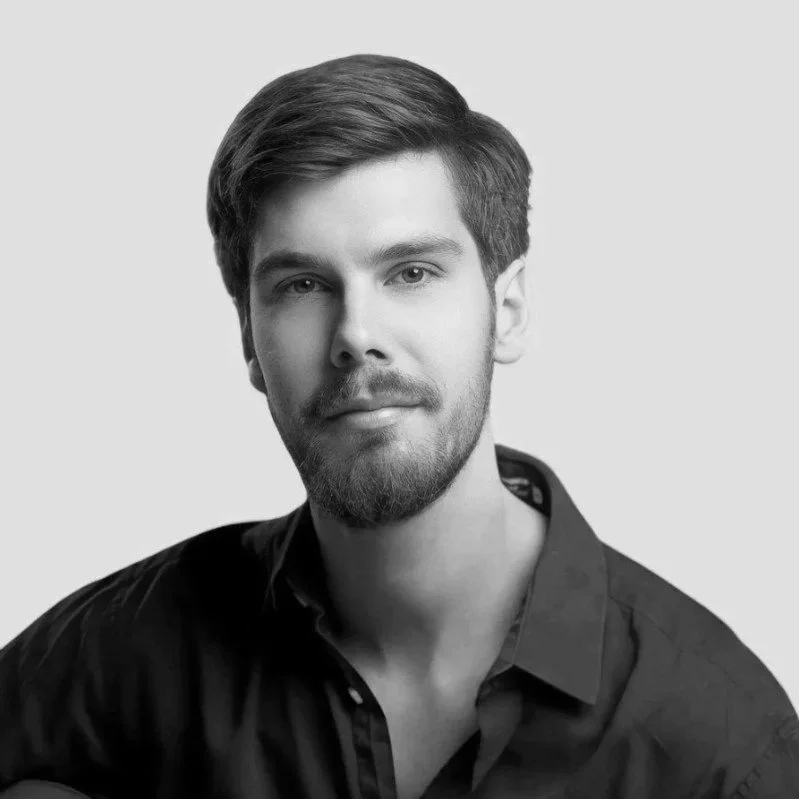 Black and white portrait of a young man with short hair and a beard, wearing a collared shirt, against a plain background.