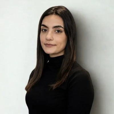 Portrait of a young woman with long dark hair, wearing a black turtleneck, against a plain white background.