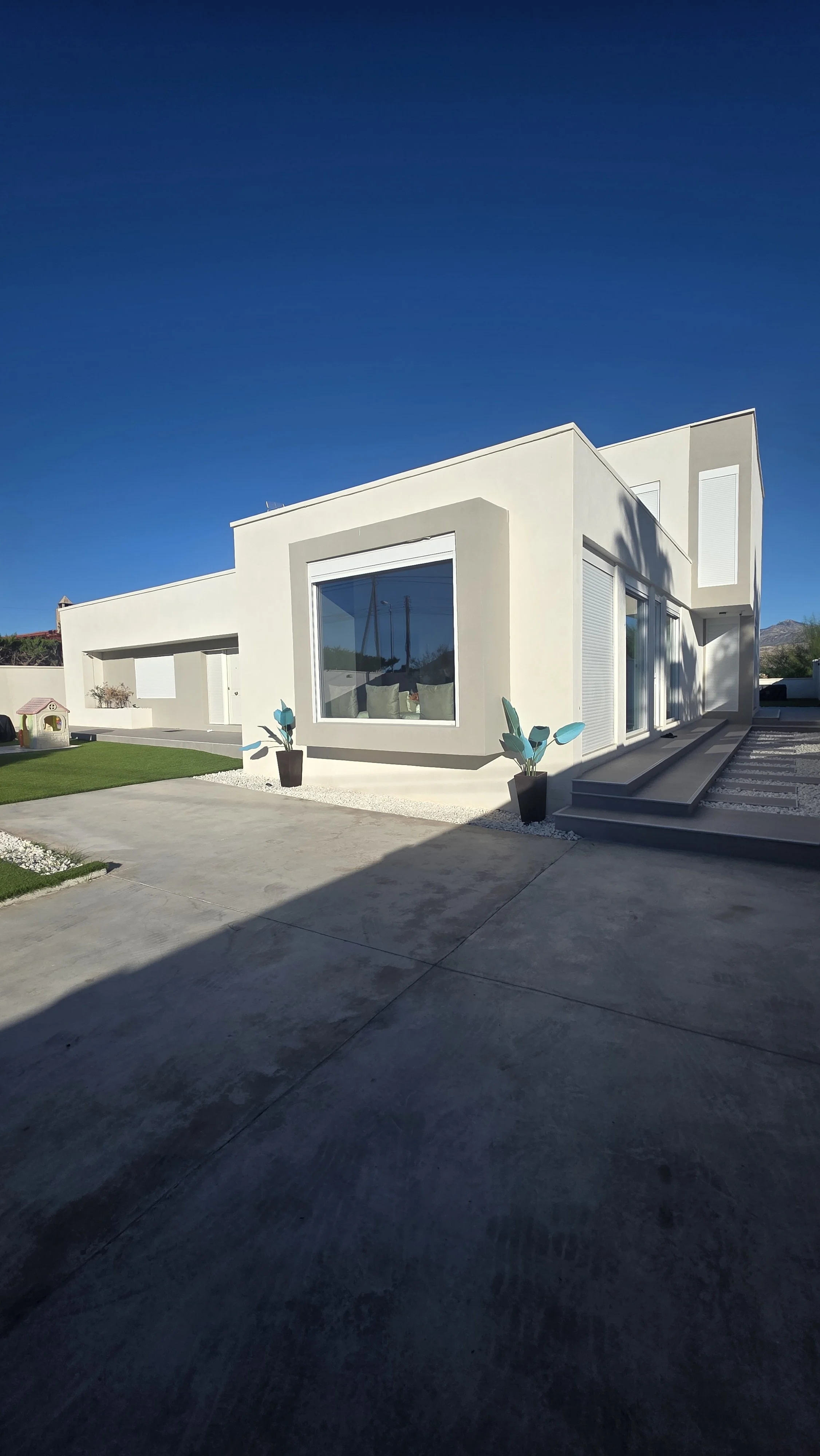 Edificio de estilo moderno con paredes blancas, grandes ventanas y plantas en macetas negras en la entrada