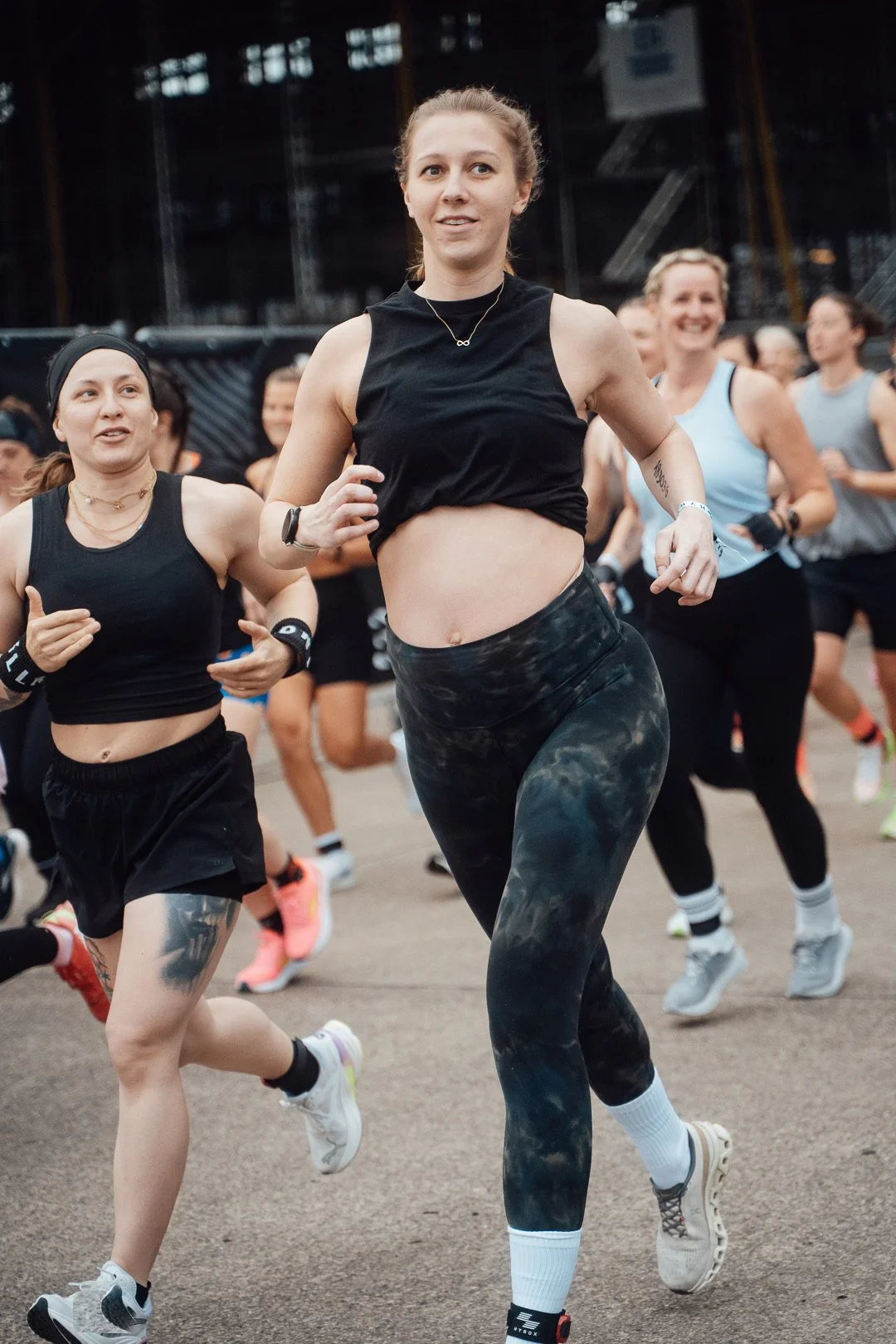 Mehrere Frauen beim Laufen bei einem Laufereignis, mit Fokus auf eine Frau in schwarzen Leggings und einem schwarzen Top, die in einer Gruppe läuft.