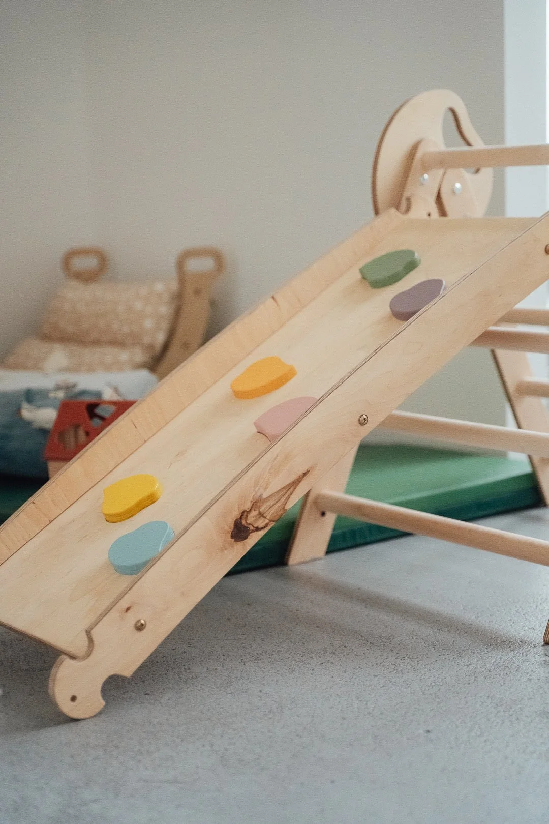 Eine Holzrutsche mit bunten Steinchen in einem Raum, im Hintergrund ein beige-polsternder Sitz.