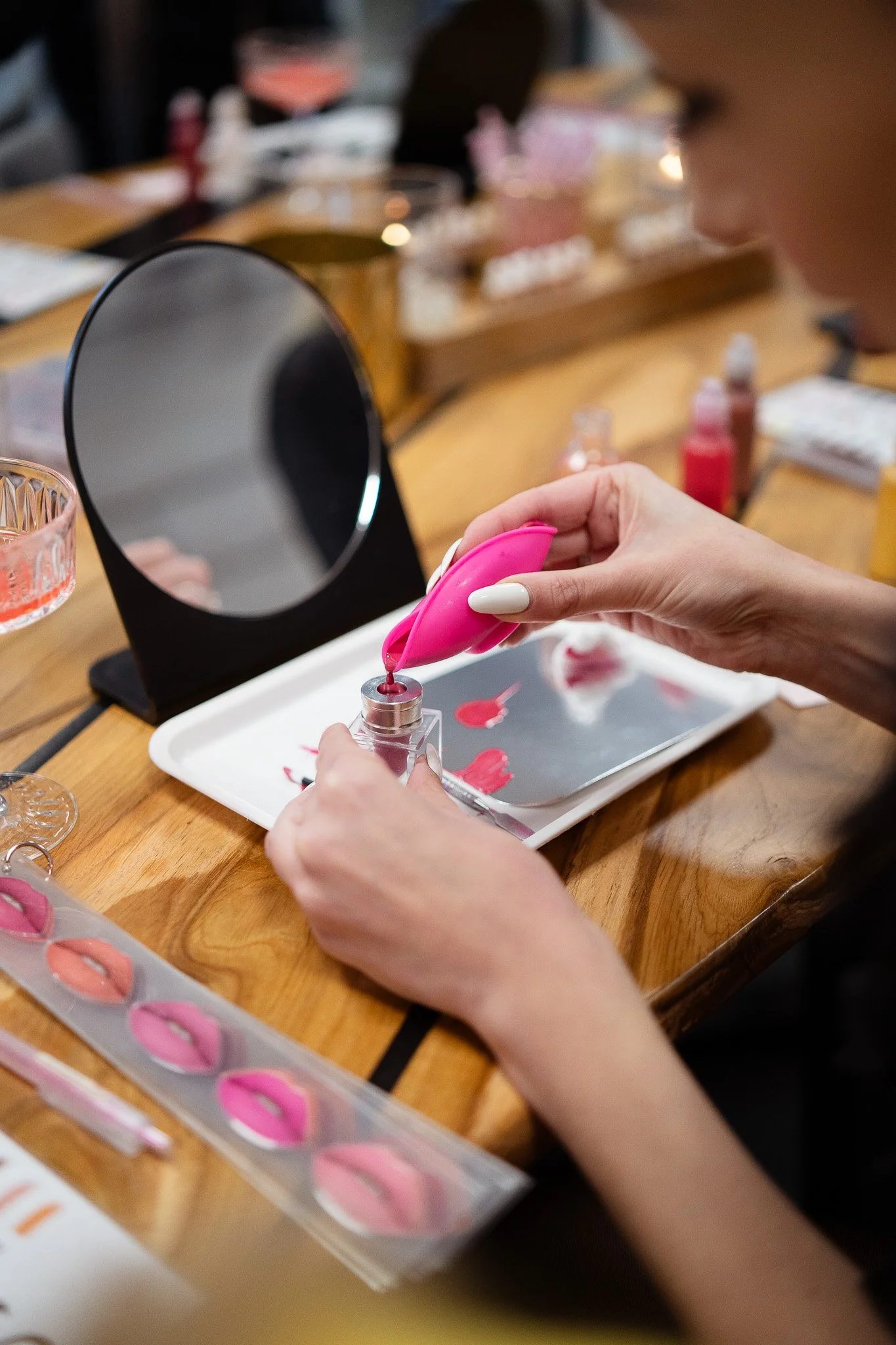 Person filling a small bottle with pink nail polish at a nail art station with a mirror and various nail polish bottles around.