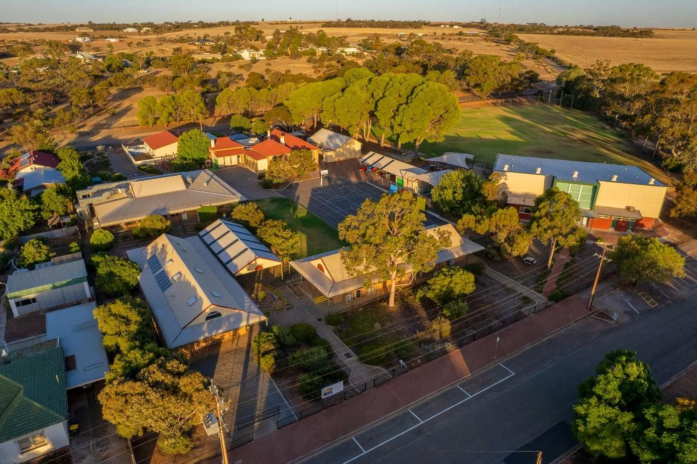 Aerial view of a small town with residential houses, trees, parking lot, and a sports field in the background during daylight.