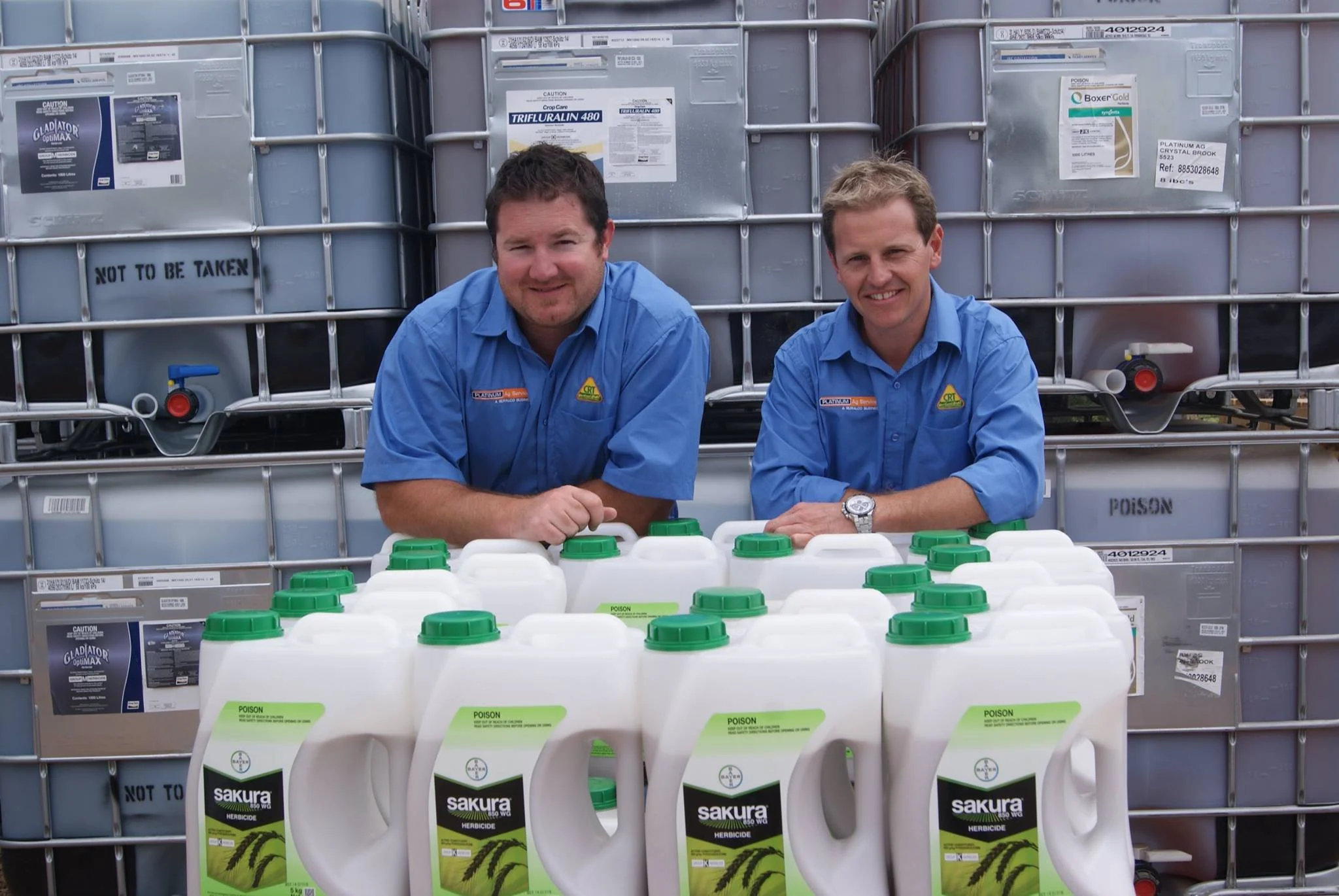 two men standing next to tubs of ag chemicals smiling at camera