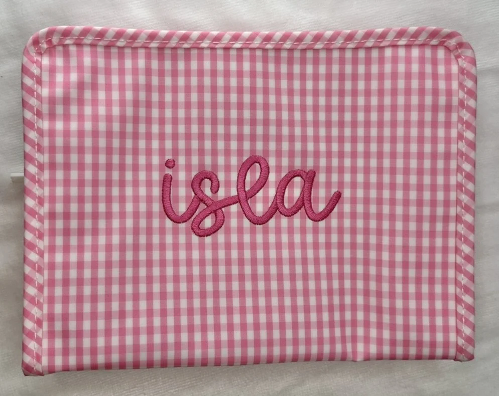 A pink and white gingham-patterned fabric box with the name 'Isla' embroidered in pink script on the front.