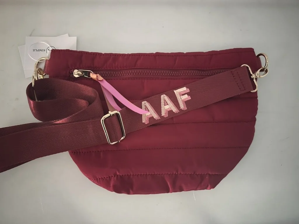 A red quilted bag with a zipper and a brown strap decorated with pink letters AAF.