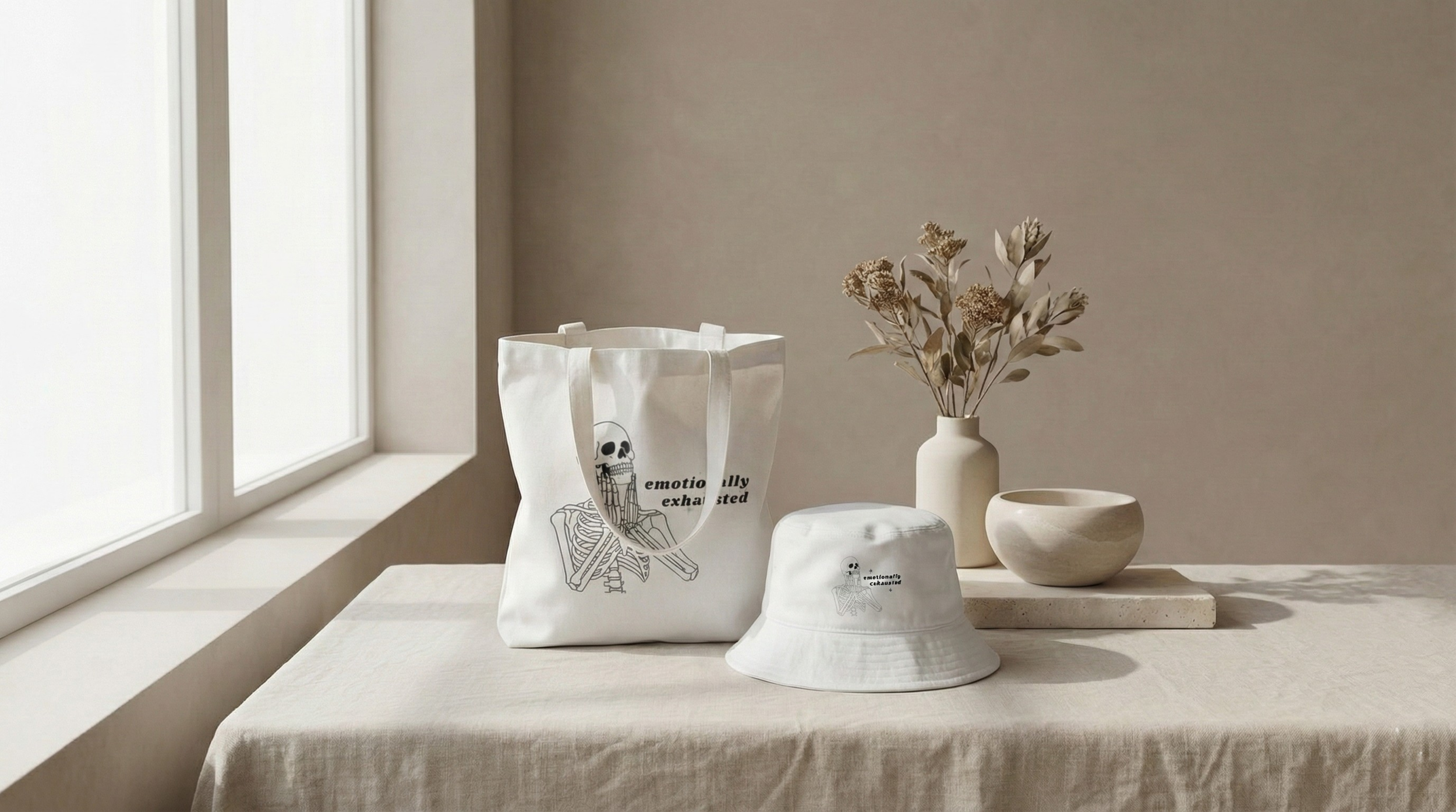 Emotionally Exhausted canvas tote bag and matching bucket hat featuring a skeleton illustration, styled in a neutral, minimalist interior with soft natural light.