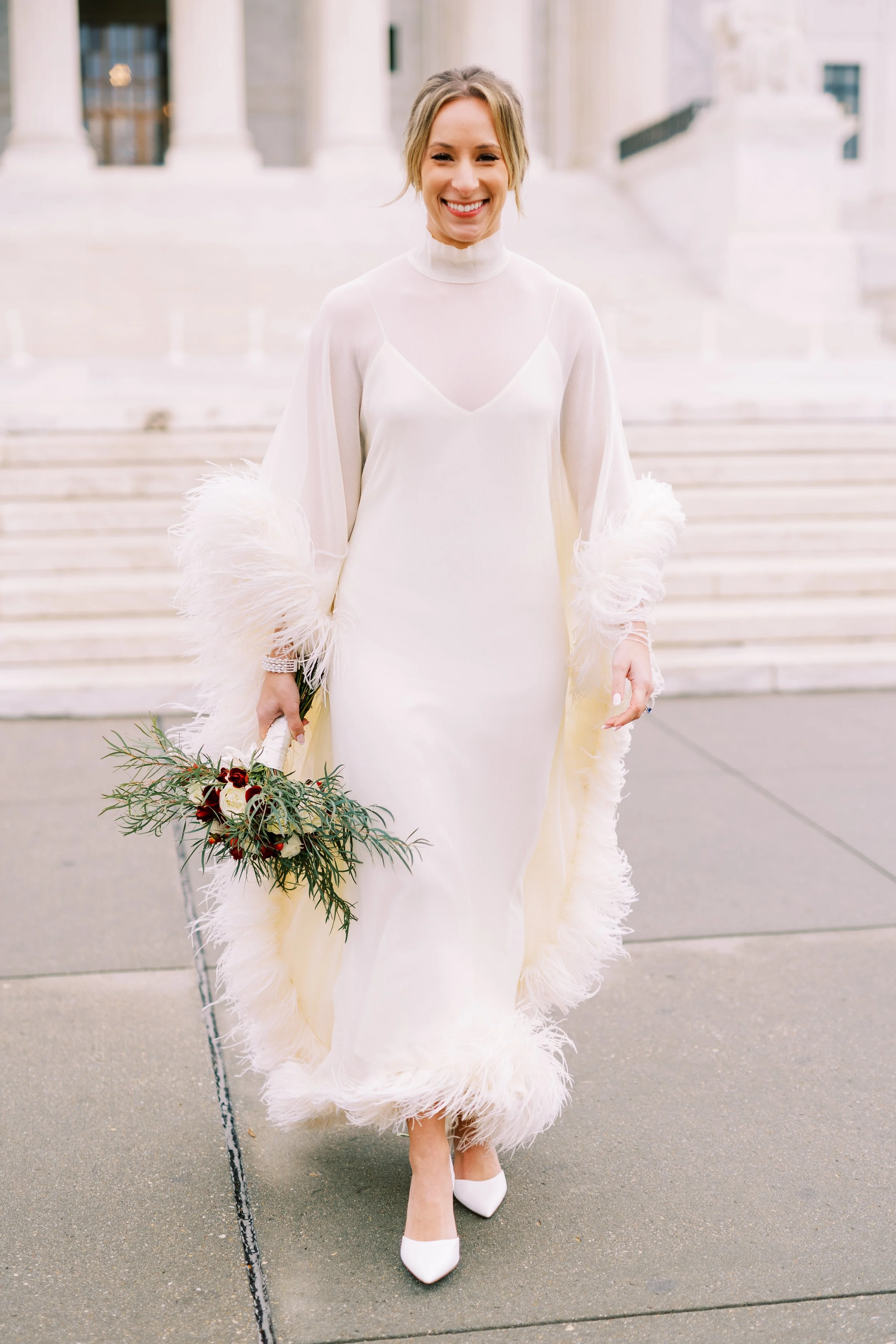 Bride walking on a city plaza carrying her greenery bouquet, feathered sleeve detail on her dress