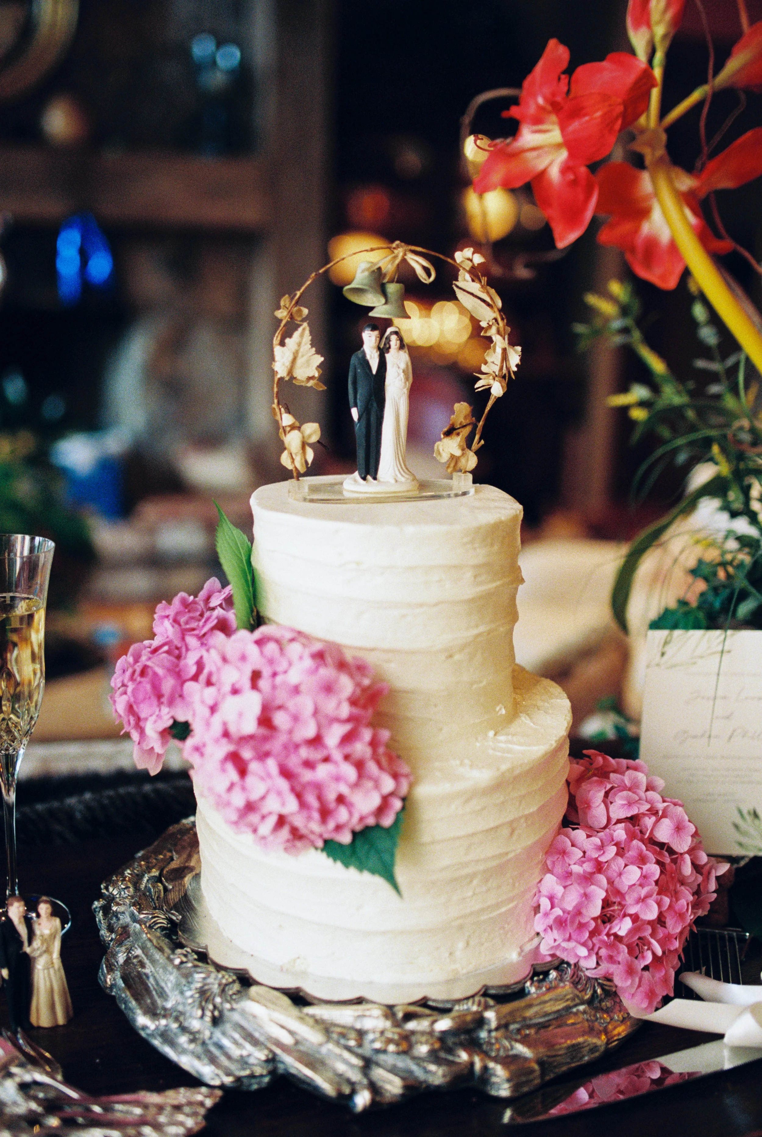 White two-tier wedding cake decorated with pink hydrangeas and a boat-shaped topper