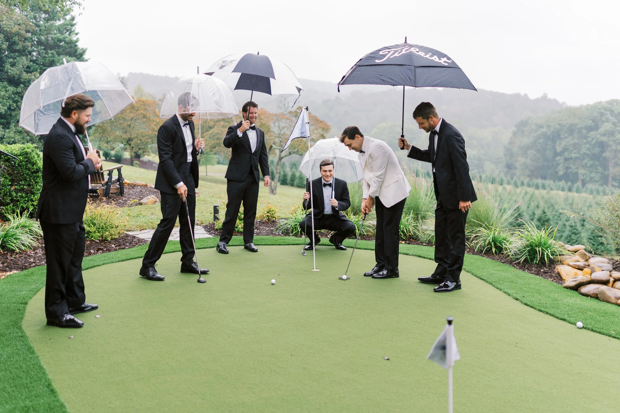 Groomsmen gathered with umbrellas on the golf green in the rain