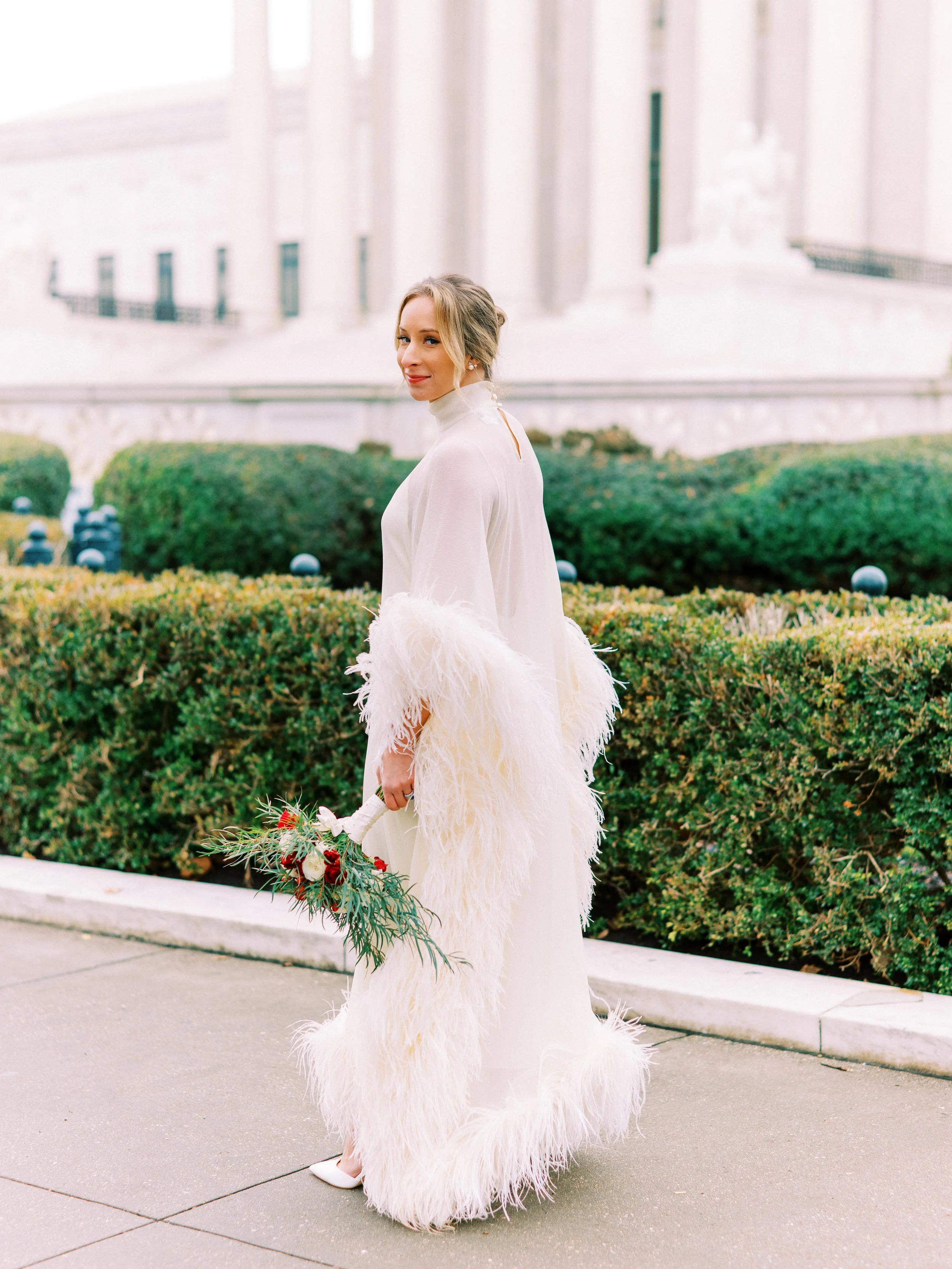 Bride walking solo along a garden path lined with hedges
