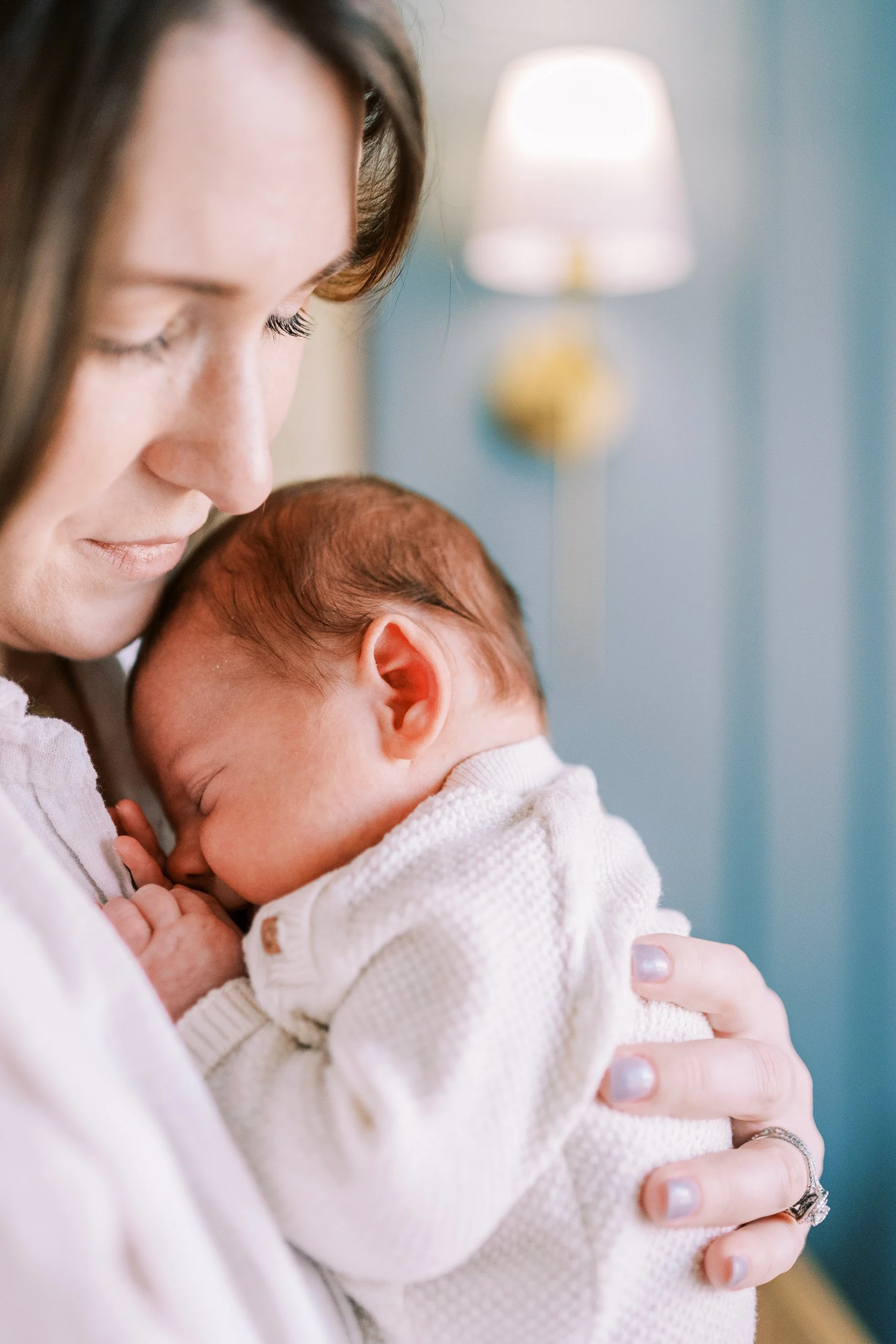 Mother kissing her sleeping newborn's forehead in soft nursery light, Roswell, Georgia