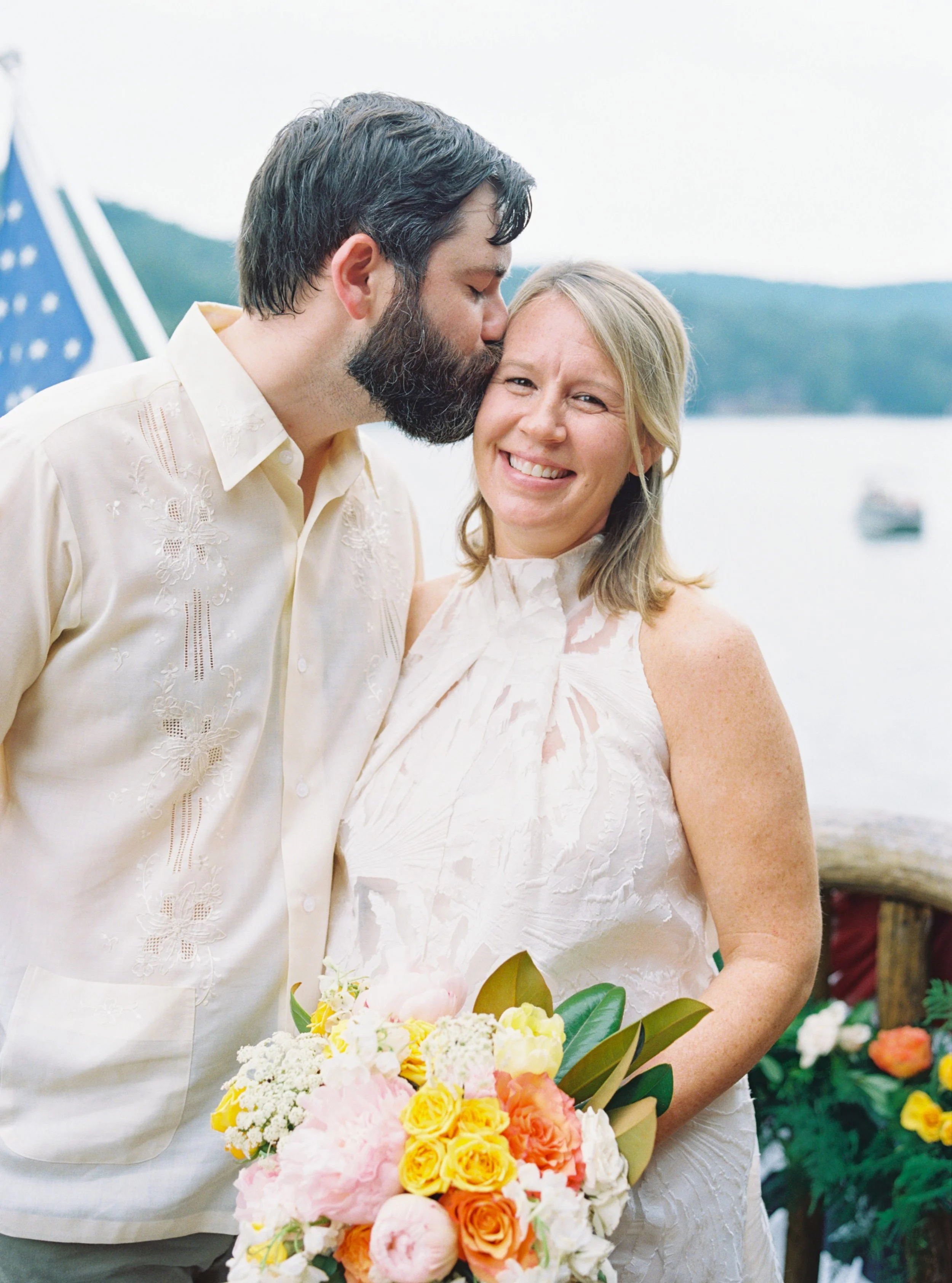 Groom kissing the bride's cheek as she holds a colorful bouquet, both smiling