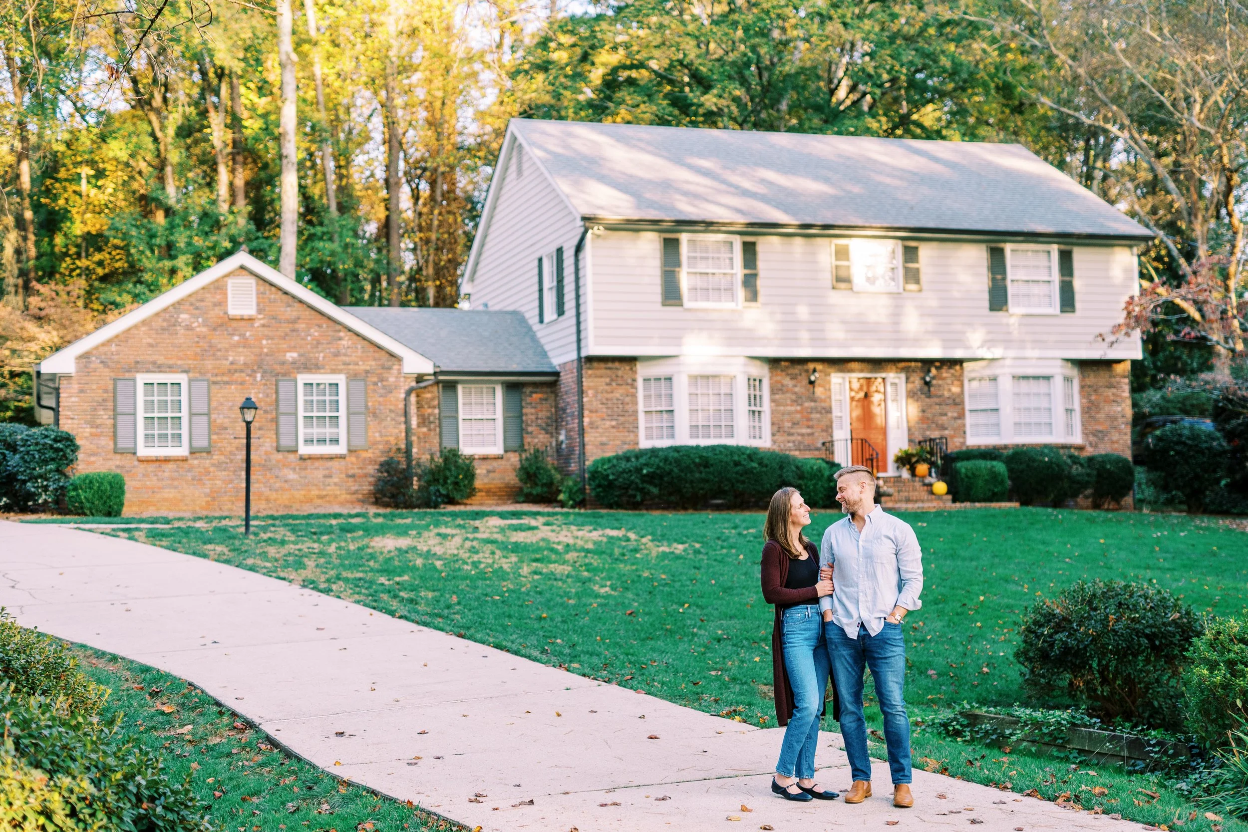 Wide view of Holly and Chris standing in front of their brick colonial home in Dunwoody, Georgia