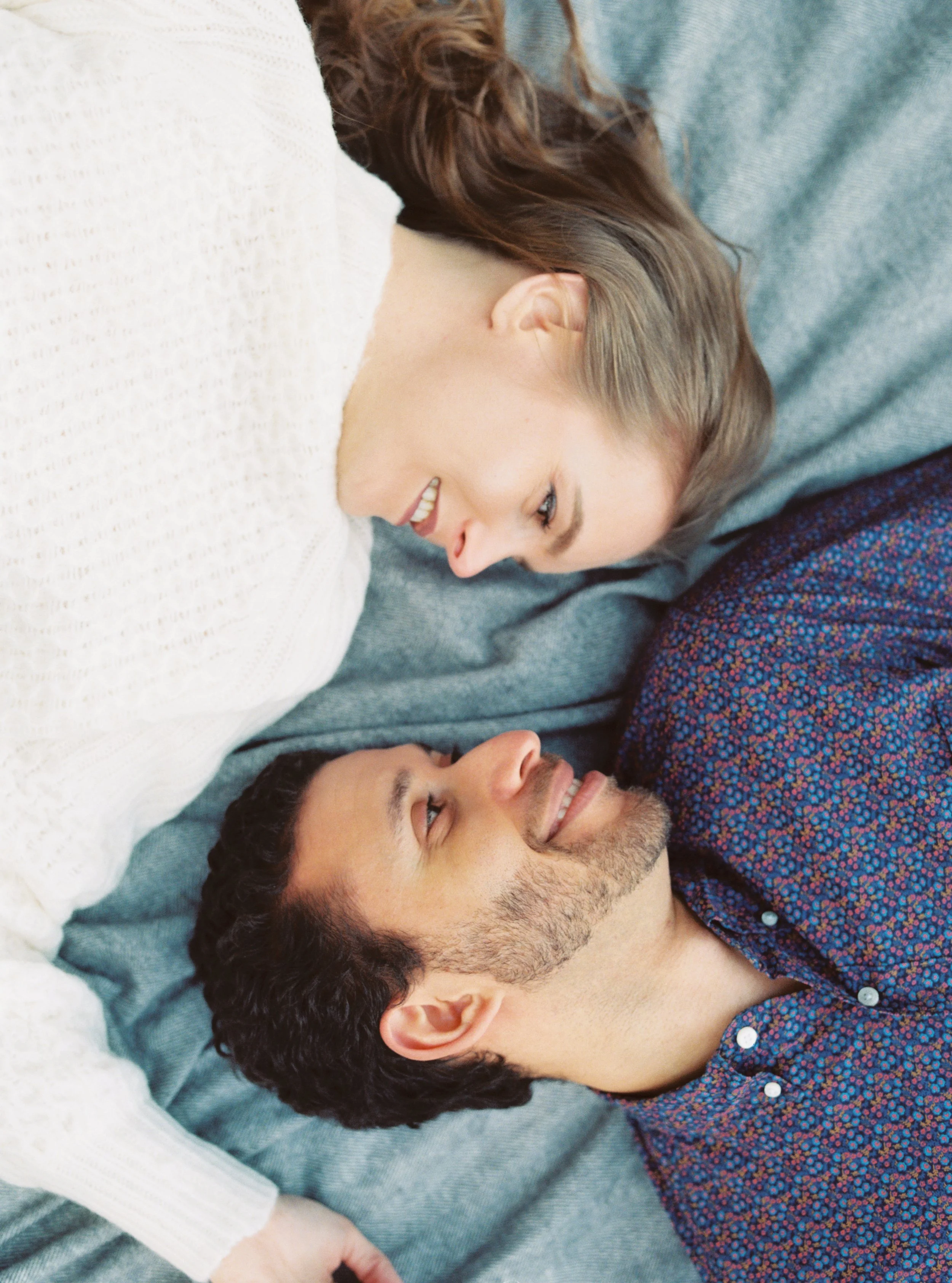 Overhead shot of the couple lying close together, faces nearly touching, smiling