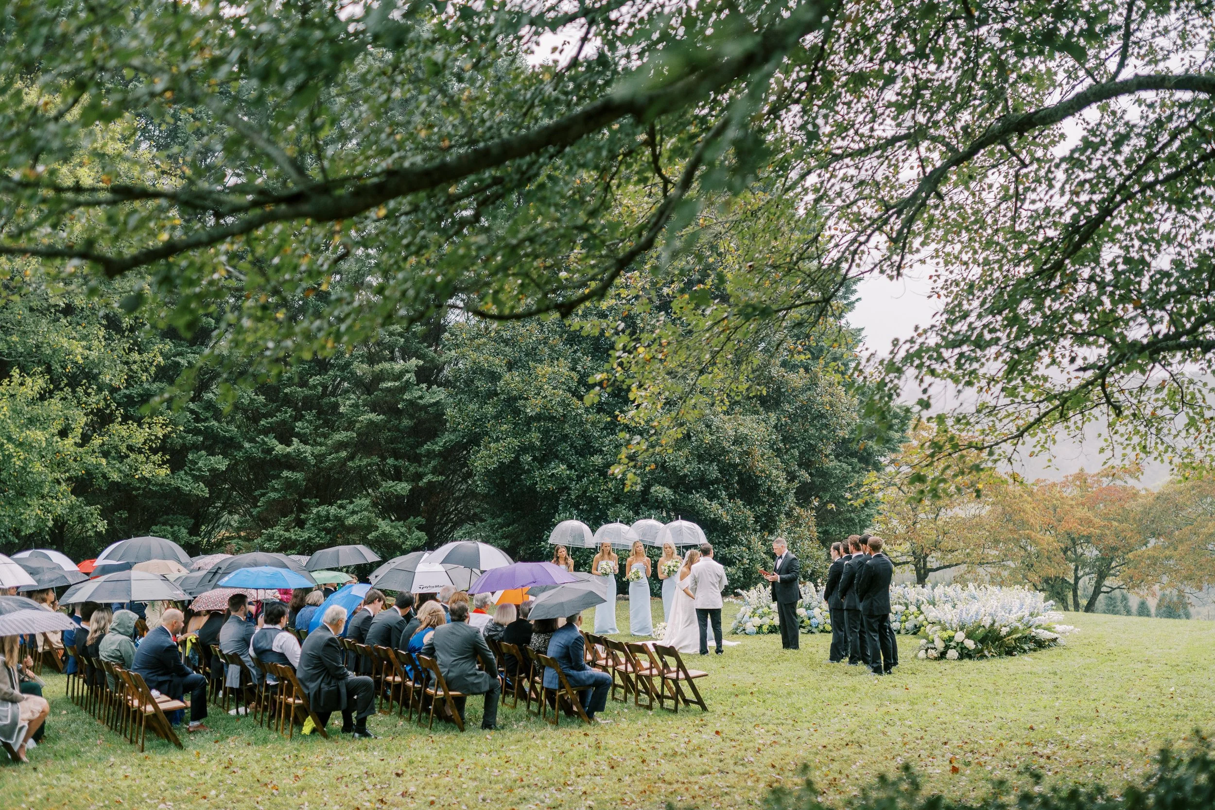 Guests with colorful umbrellas watching the ceremony under a tree