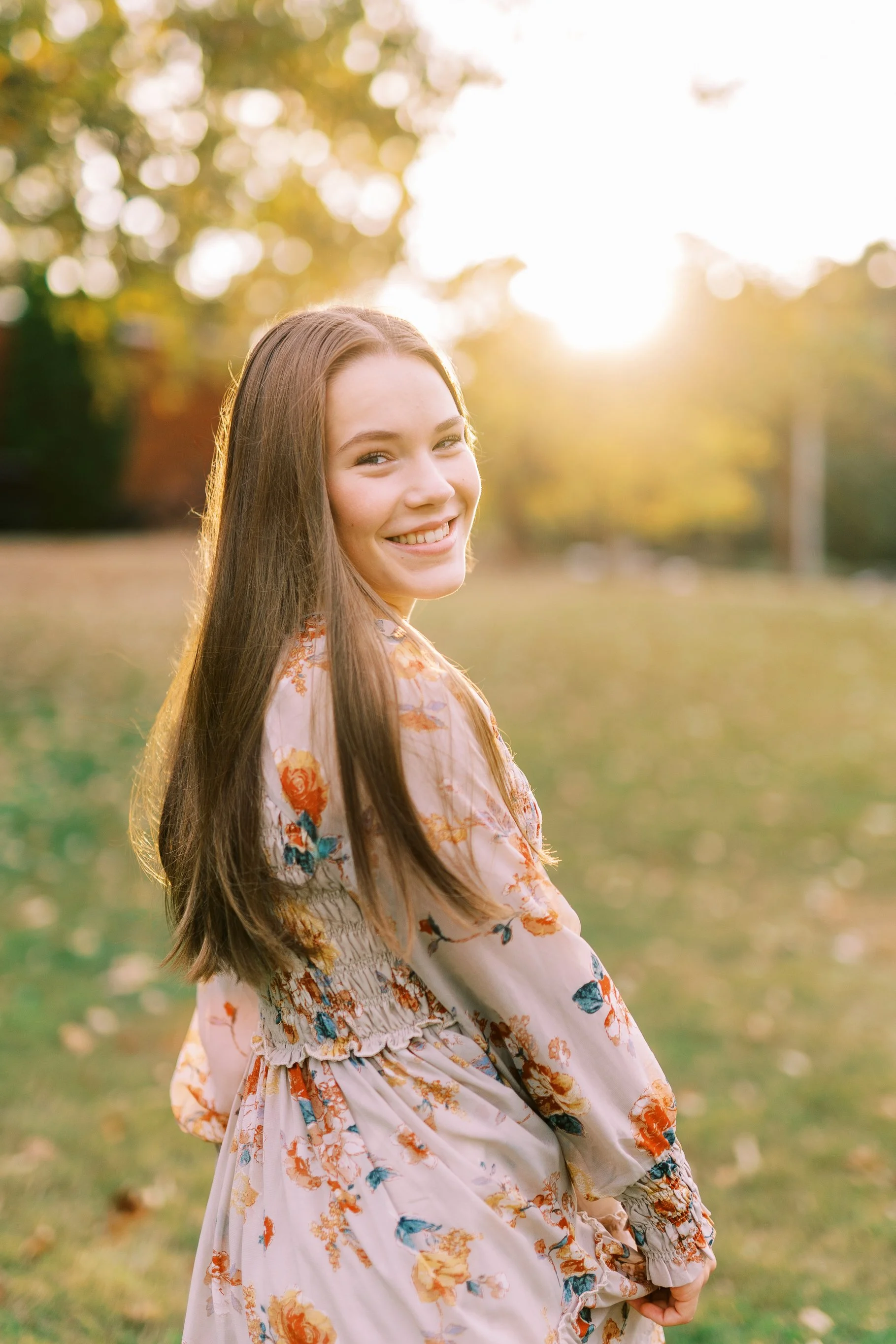 Senior portrait of Hannah smiling in golden hour light in a floral dress at Kennesaw Mountain Battlefield Park in Kennesaw, Georgia