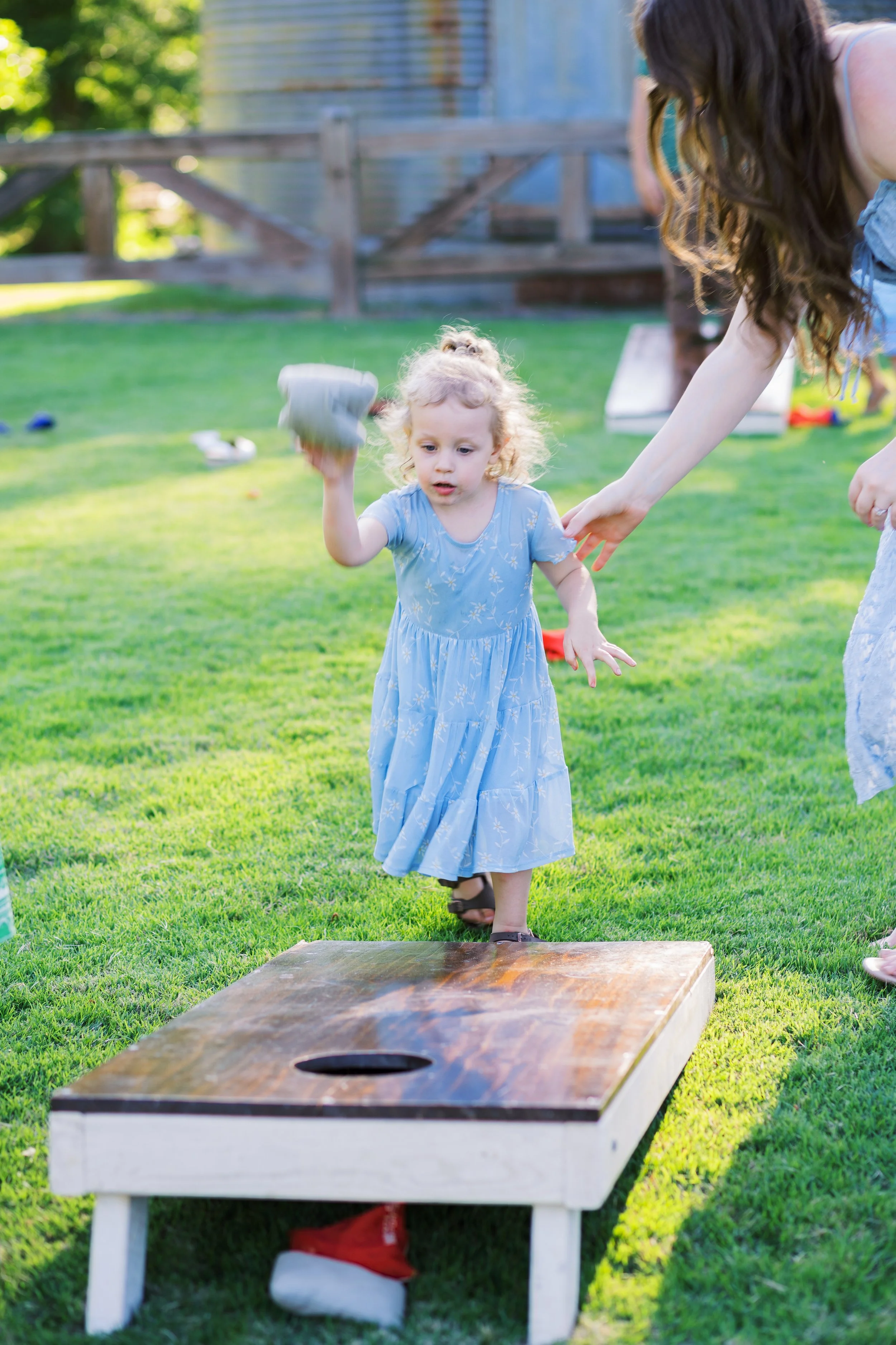 Young guest tossing a bean bag while playing cornhole on the lawn