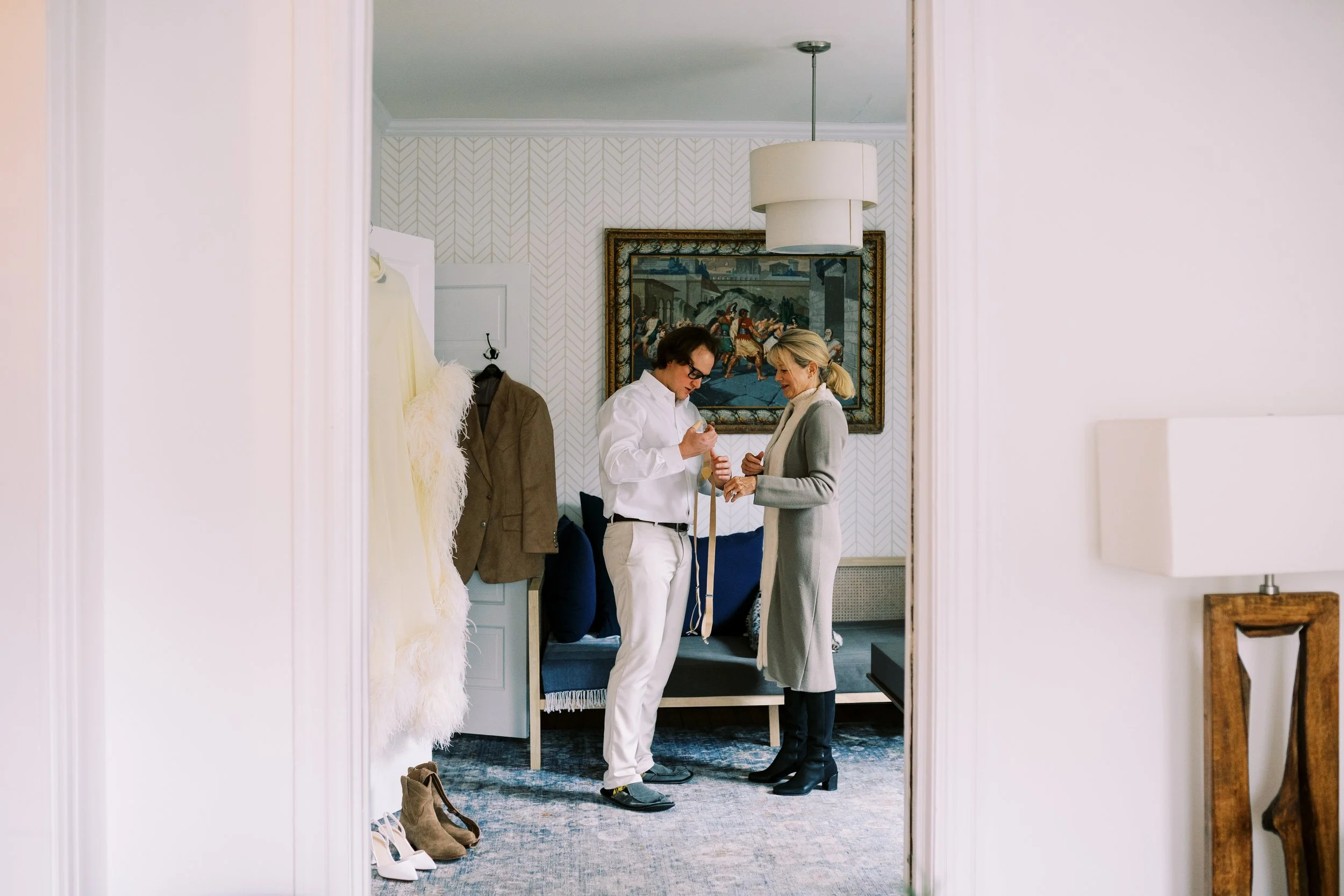 Groom having his suit adjusted while getting ready in a hotel room