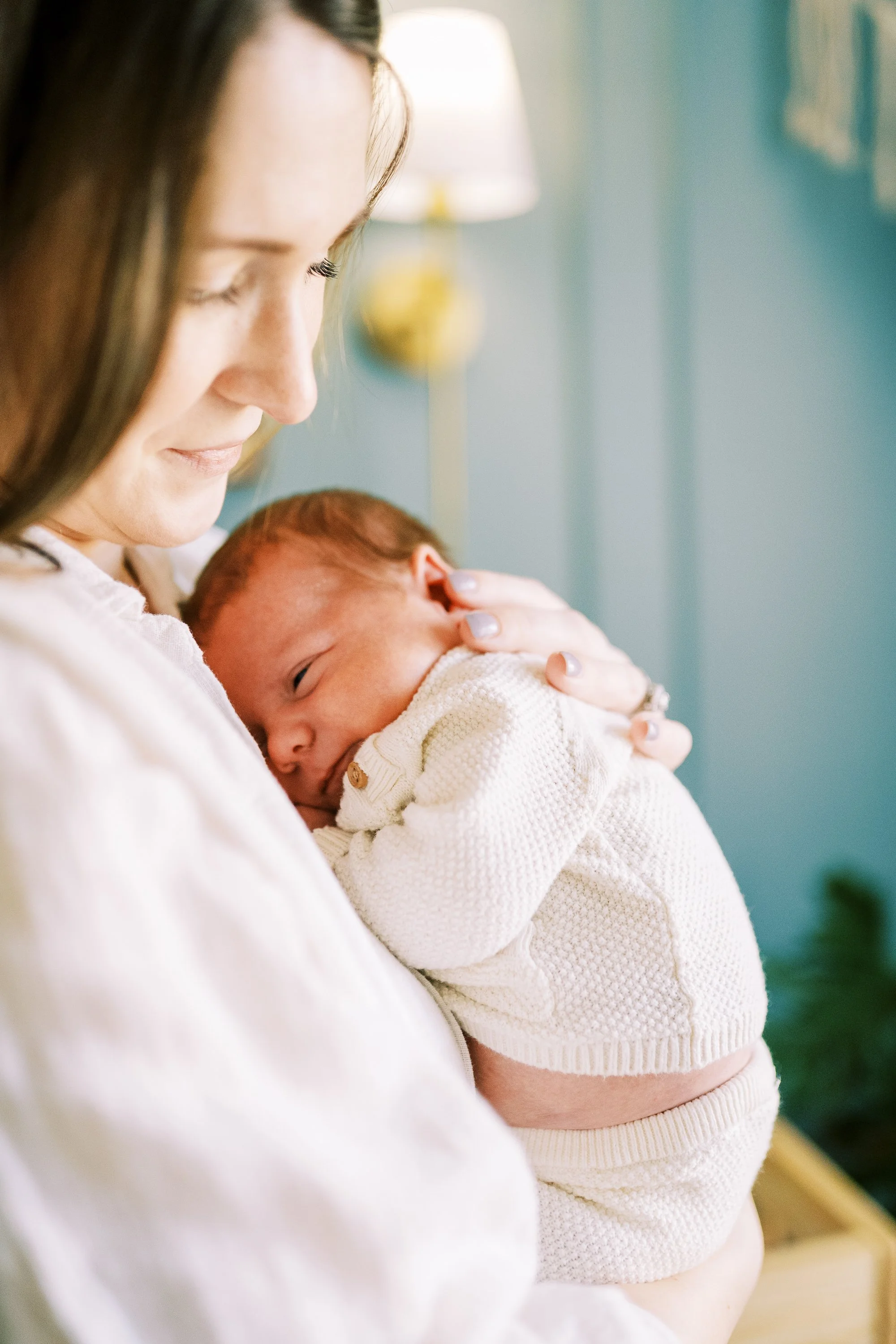 Mother standing and holding her newborn in the nursery, surrounded by plants and stuffed animals, Roswell, Georgia